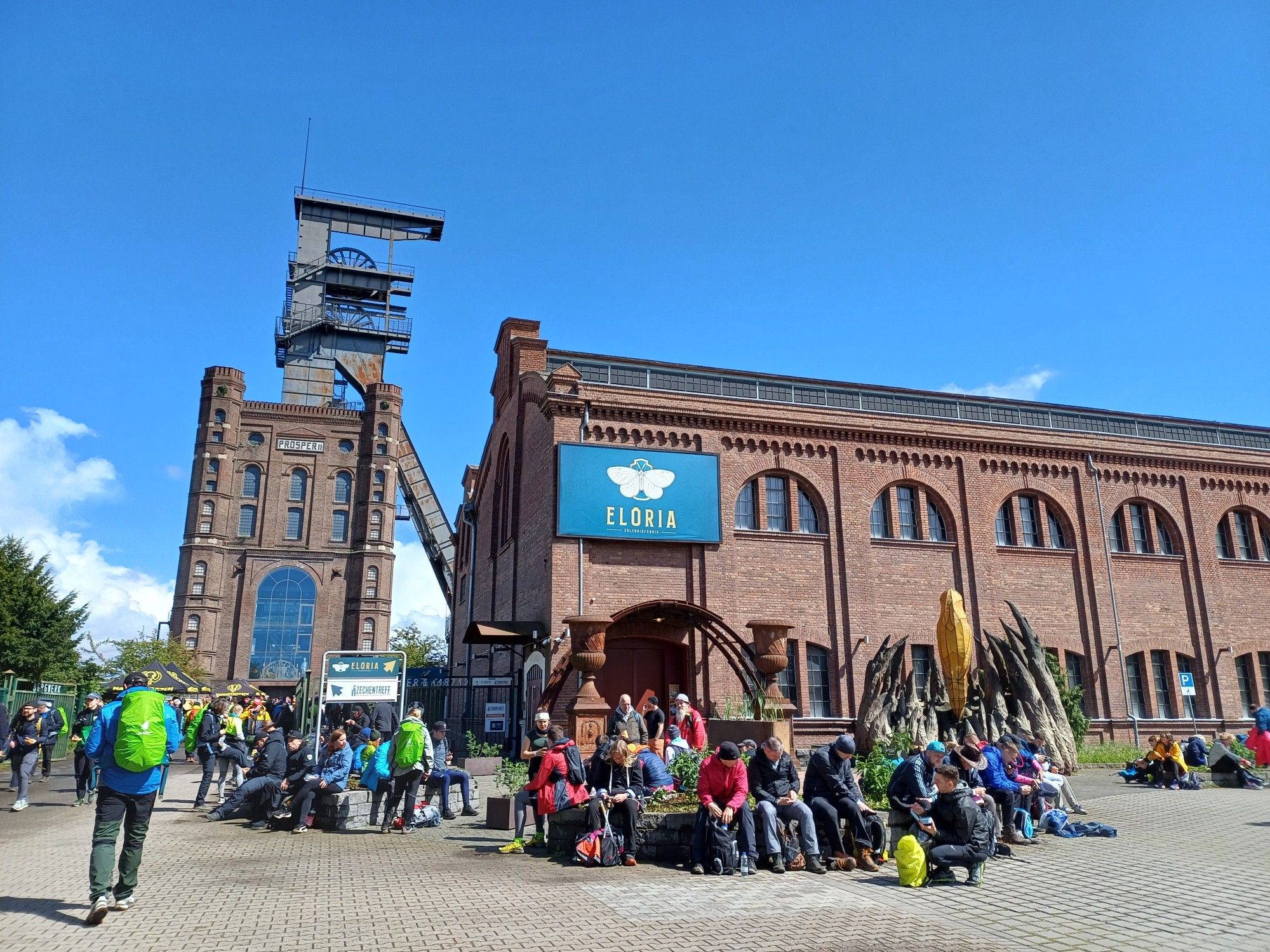 Eine alte Fabrik, steht Eloria drauf. Davor sitzen einige Wandernde