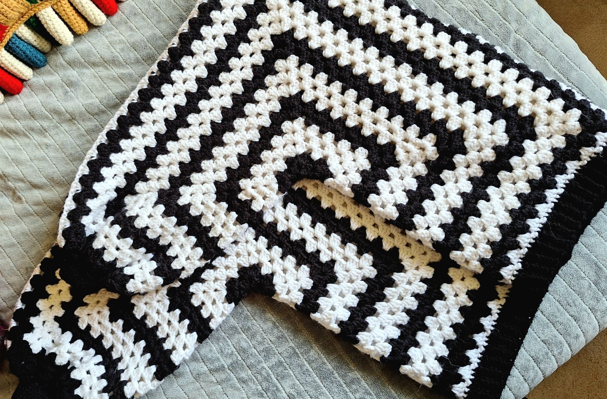 Black and white crochet sweater laying on a Grey blanket. it has alternating black and white horizontal and vertical stripes