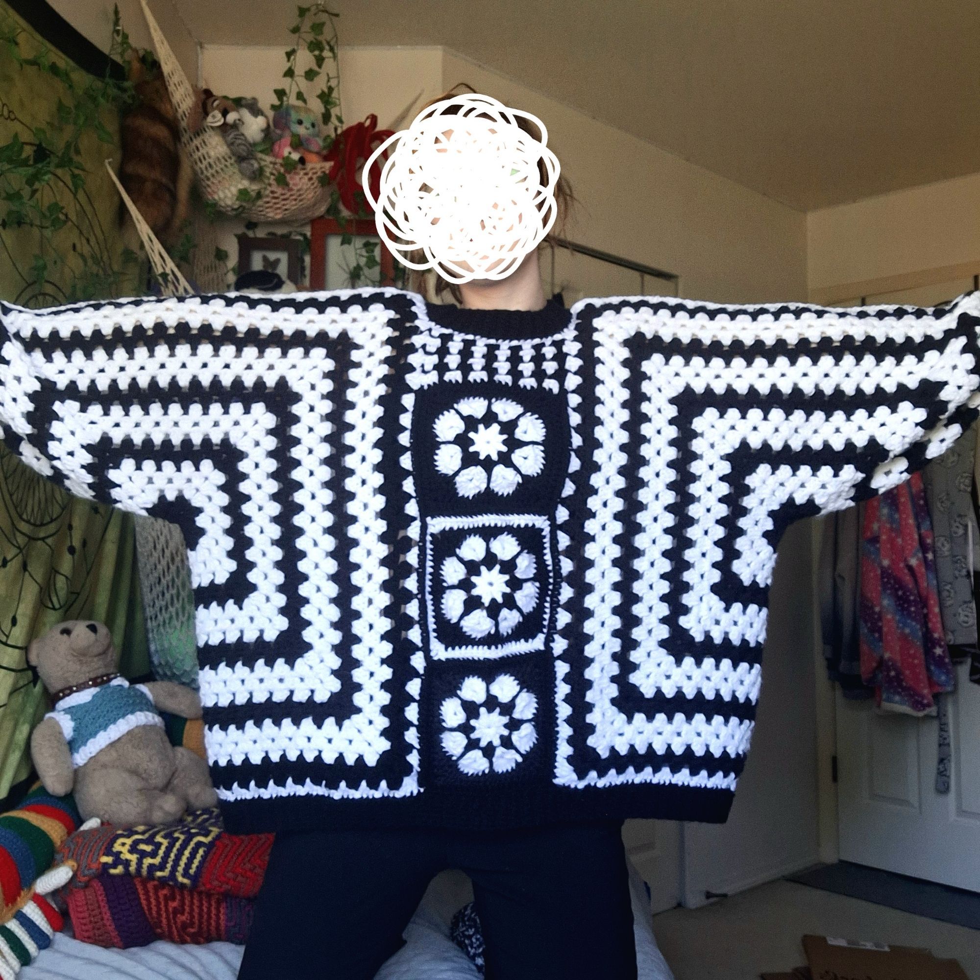 photo of a person wearing a crochet sweater. it has alternating black and white horizontal and vertical stripes, with 3 black and white flower granny squares down the middle.