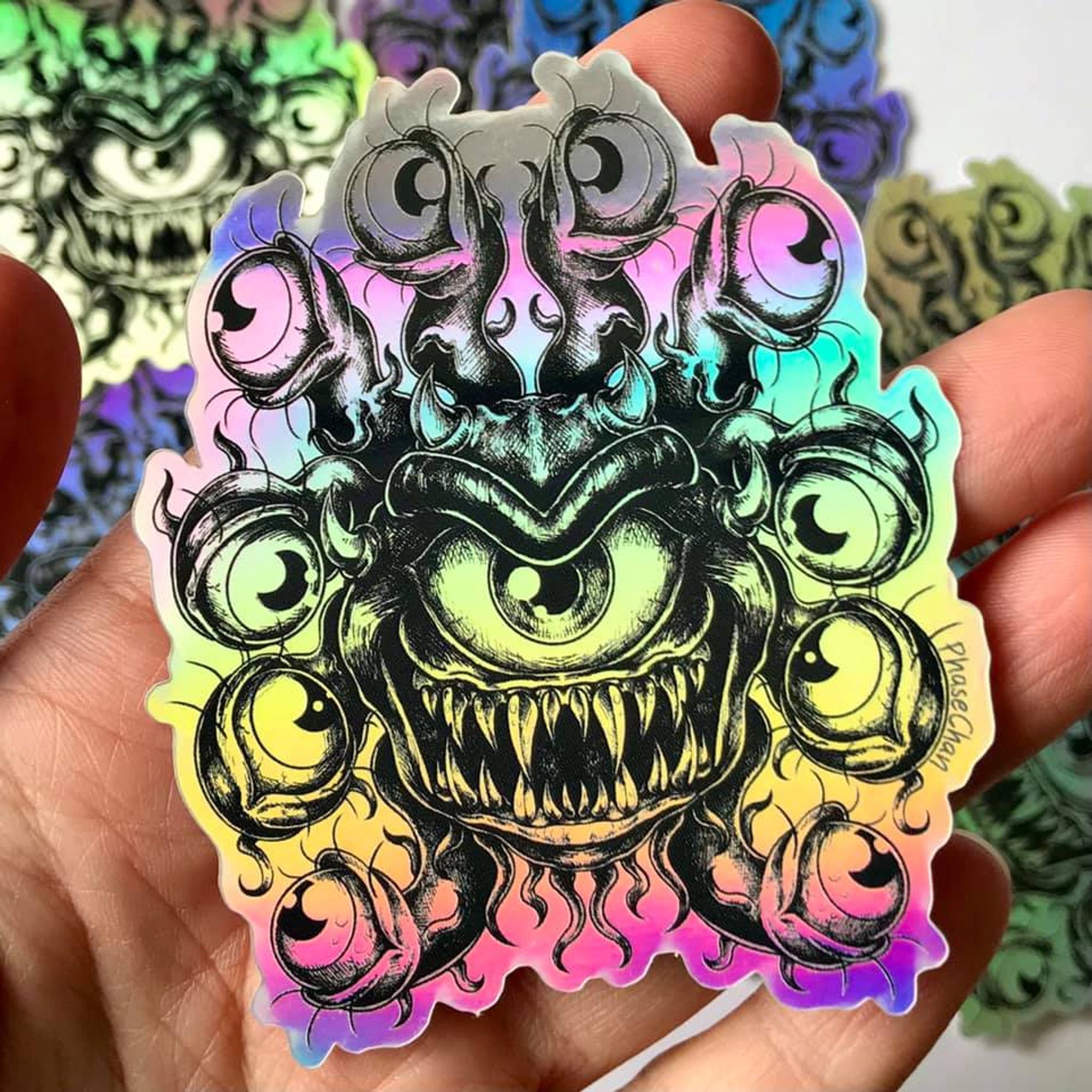 A photo of a holographic vinyl sticker featuring a beholder design. The illustration is in black and white, and this allows the holographic background to shine through.