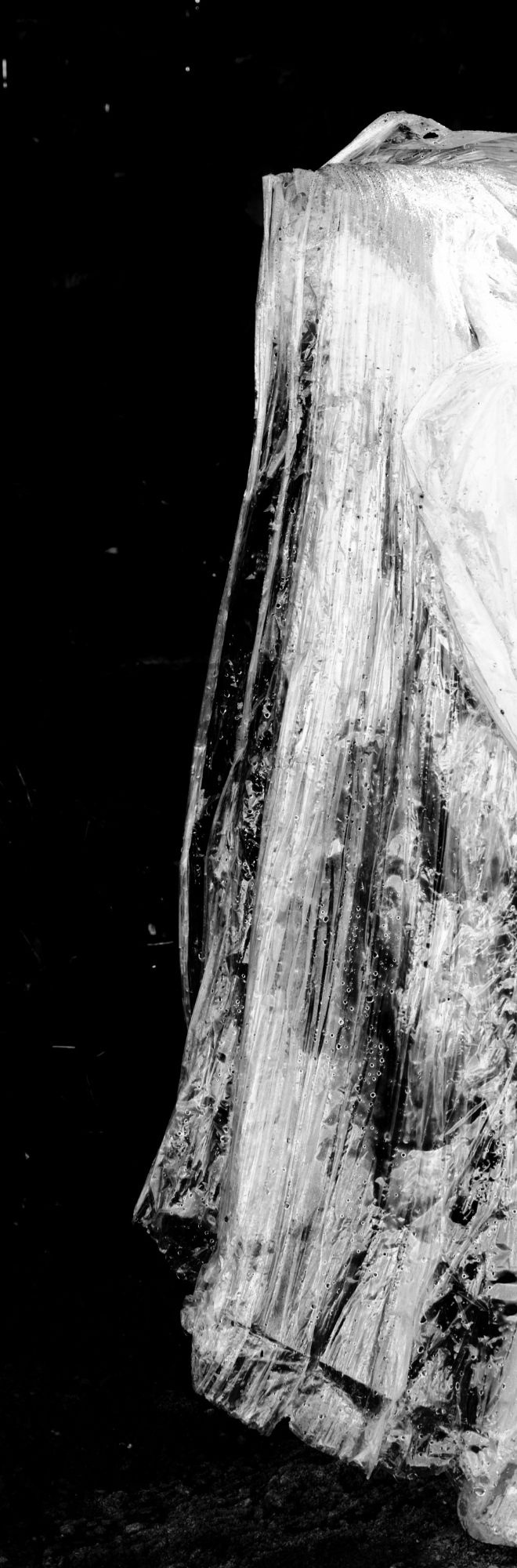 Black and white image of plastic that looks like a white dress against dark background.