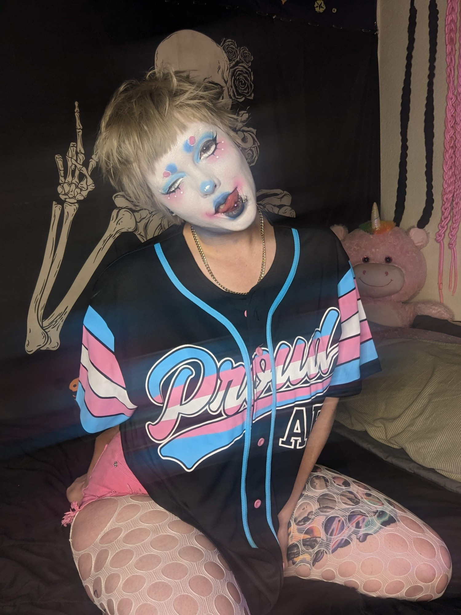 beetle in soft pink and blue clown makeup with a big trans pride "Proud AF" jersey on