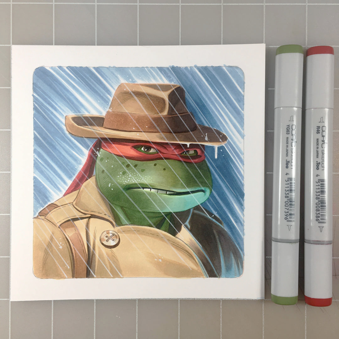 A small square marker drawing of Raphael the Teenage Mutant Ninja Turtle in a trench coat and fedora.  Rain is streaming in from the left and dripping from the brim of his hat.  To the right of the drawing are two Copic markers in green and red.