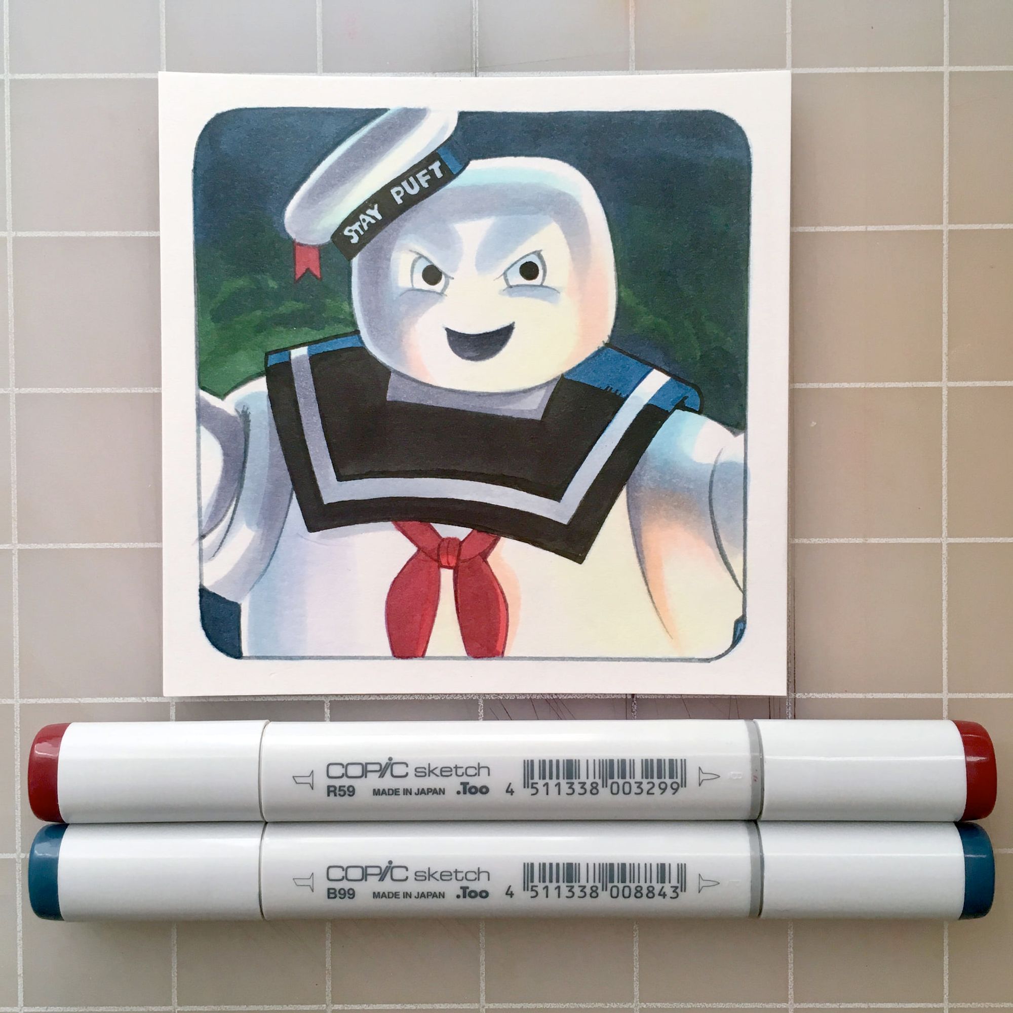 A small square drawing of the Stay Puft Marshmallow man from the movie Ghostbusters done with markers.  Two Copic markers are sitting below the drawing.