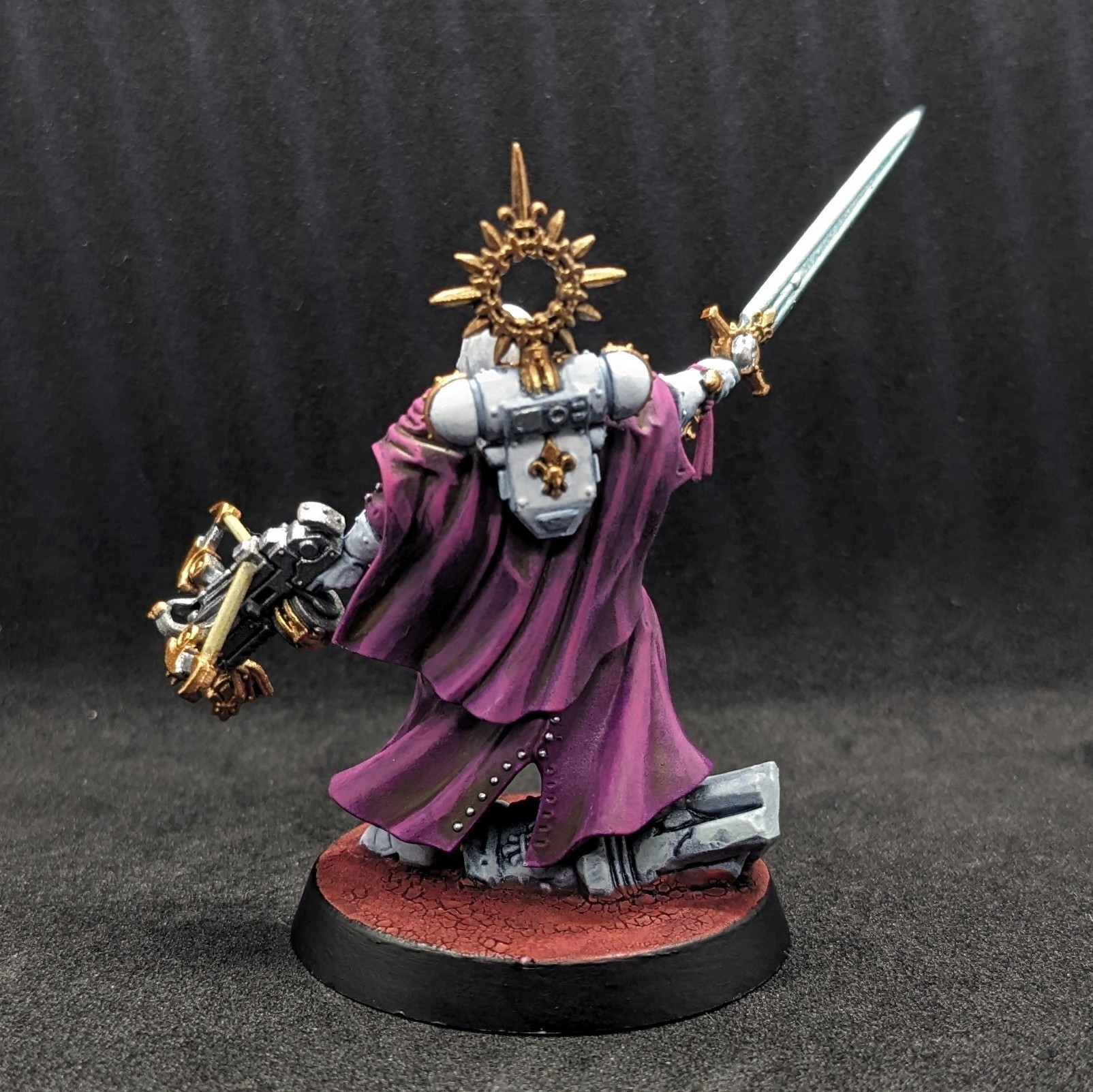 A Warhammer 40K Adepta Sororitas Canoness in white armour with purple robes, from the back