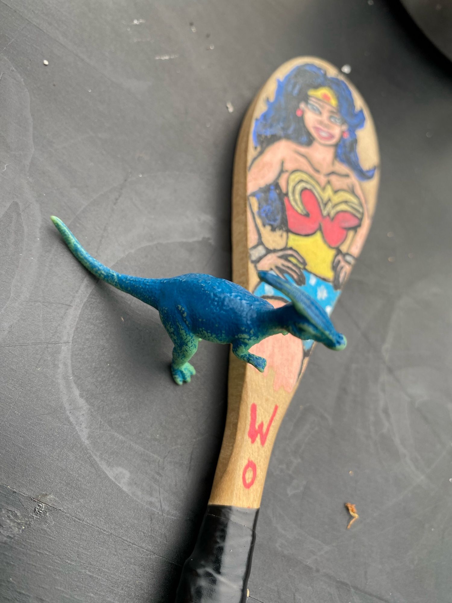 Kleiner dino neben Kochlöffel mit wonderwoman