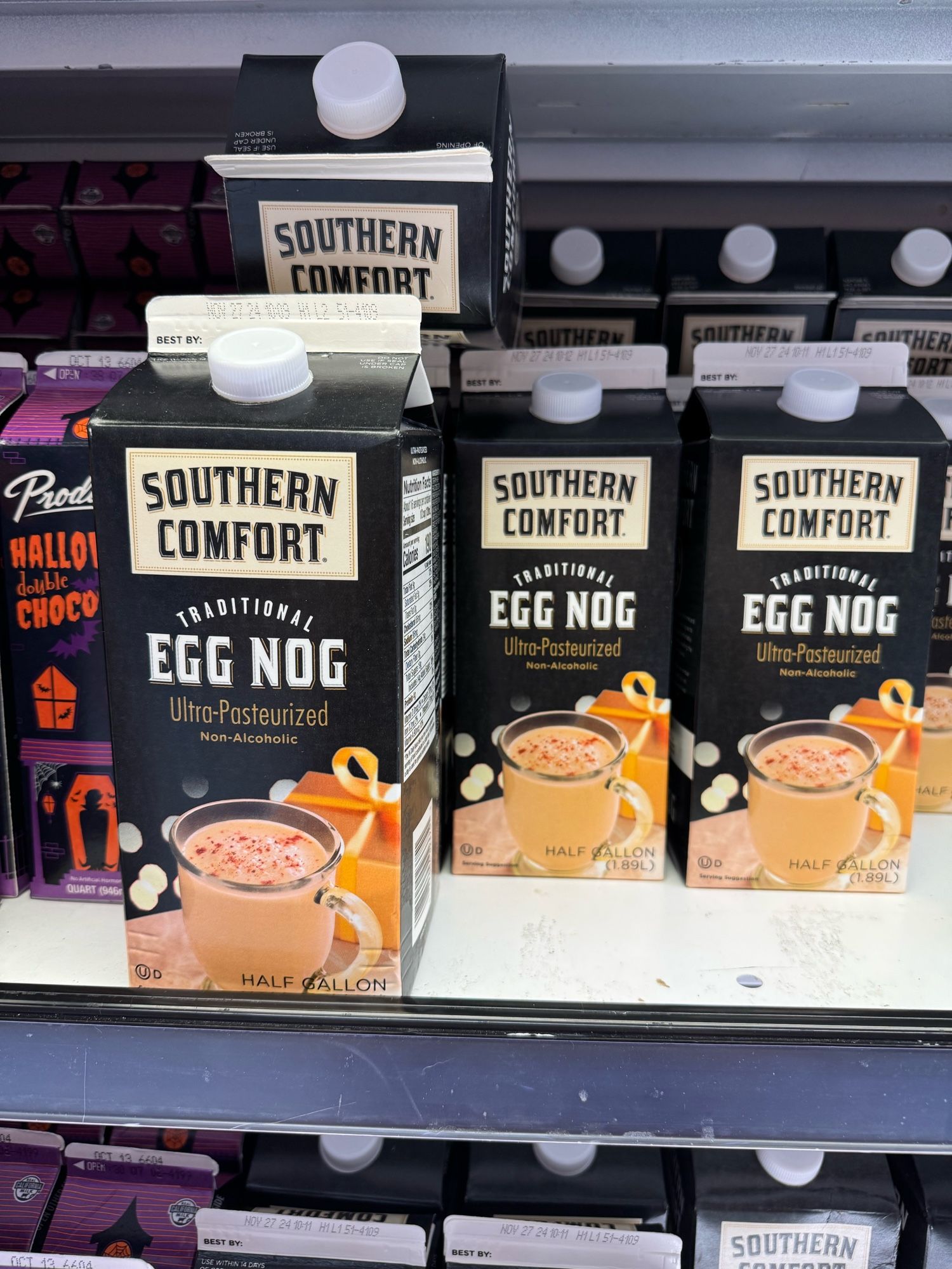 Egg nog on a shelf at the grocery store, right next to Halloween chocolate milk.