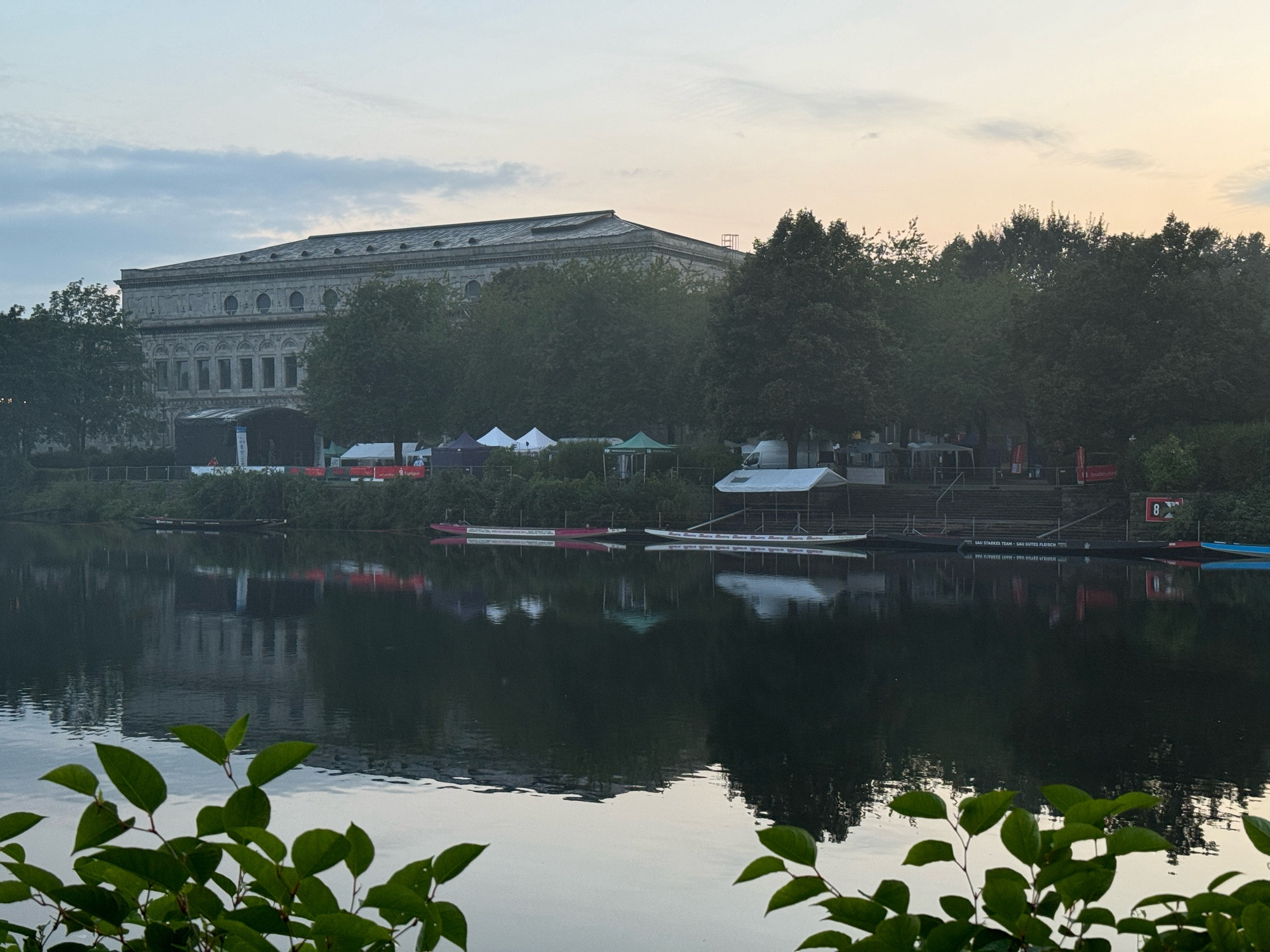 Blick auf einen Fluss mit Gebäude im Hintergrund, etwas herangezoomt sind Drachenboote zu erkennen