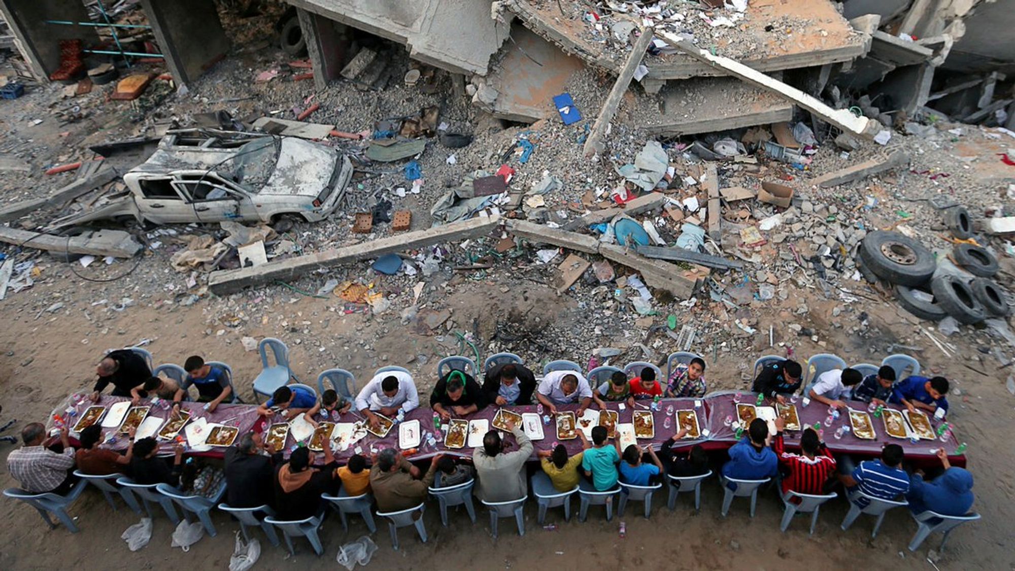 "A large group of people seated at a table among rubble"