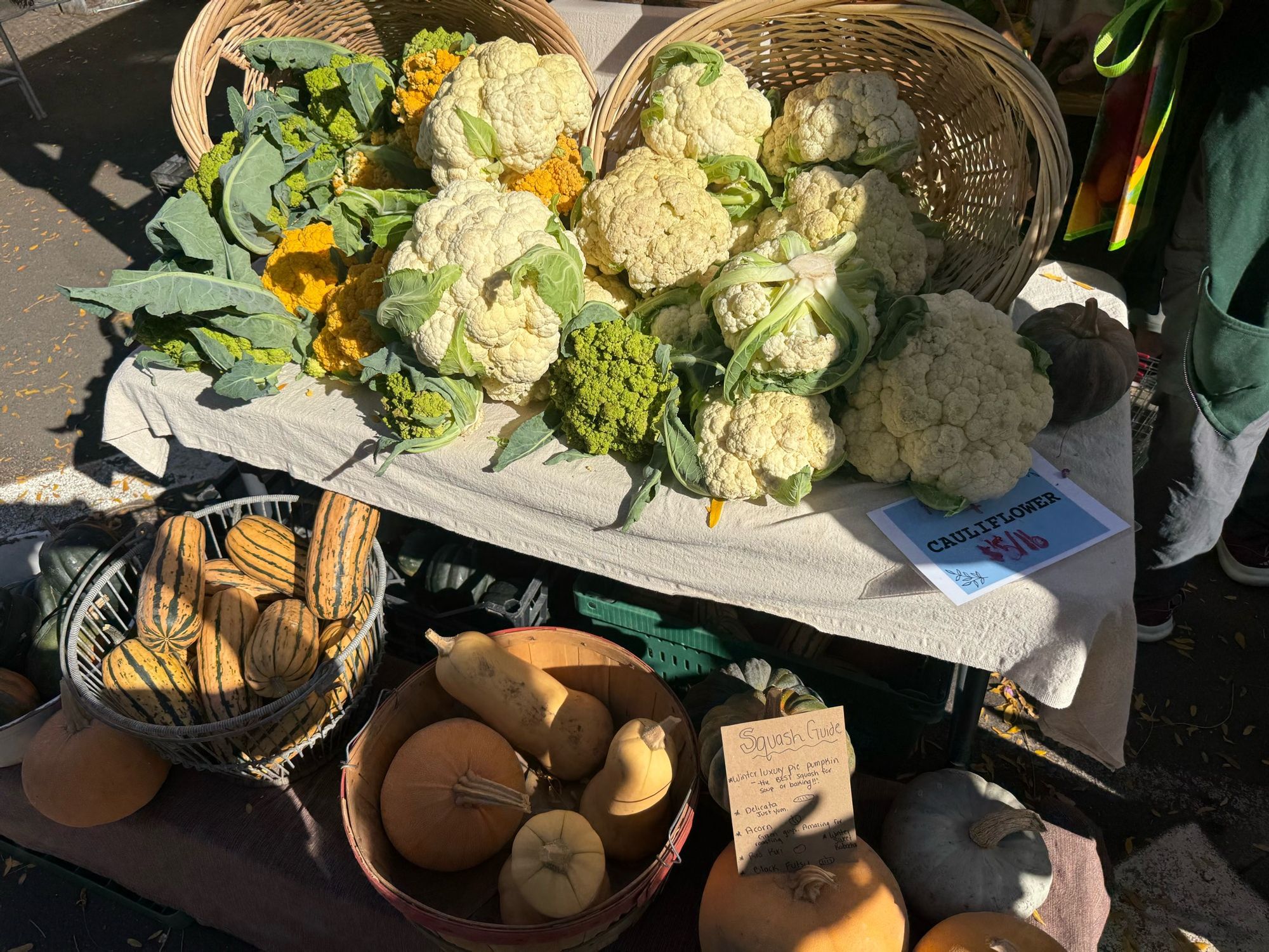 A small market stand of giant white and yellow cauliflower with winter squashes in the foreground 