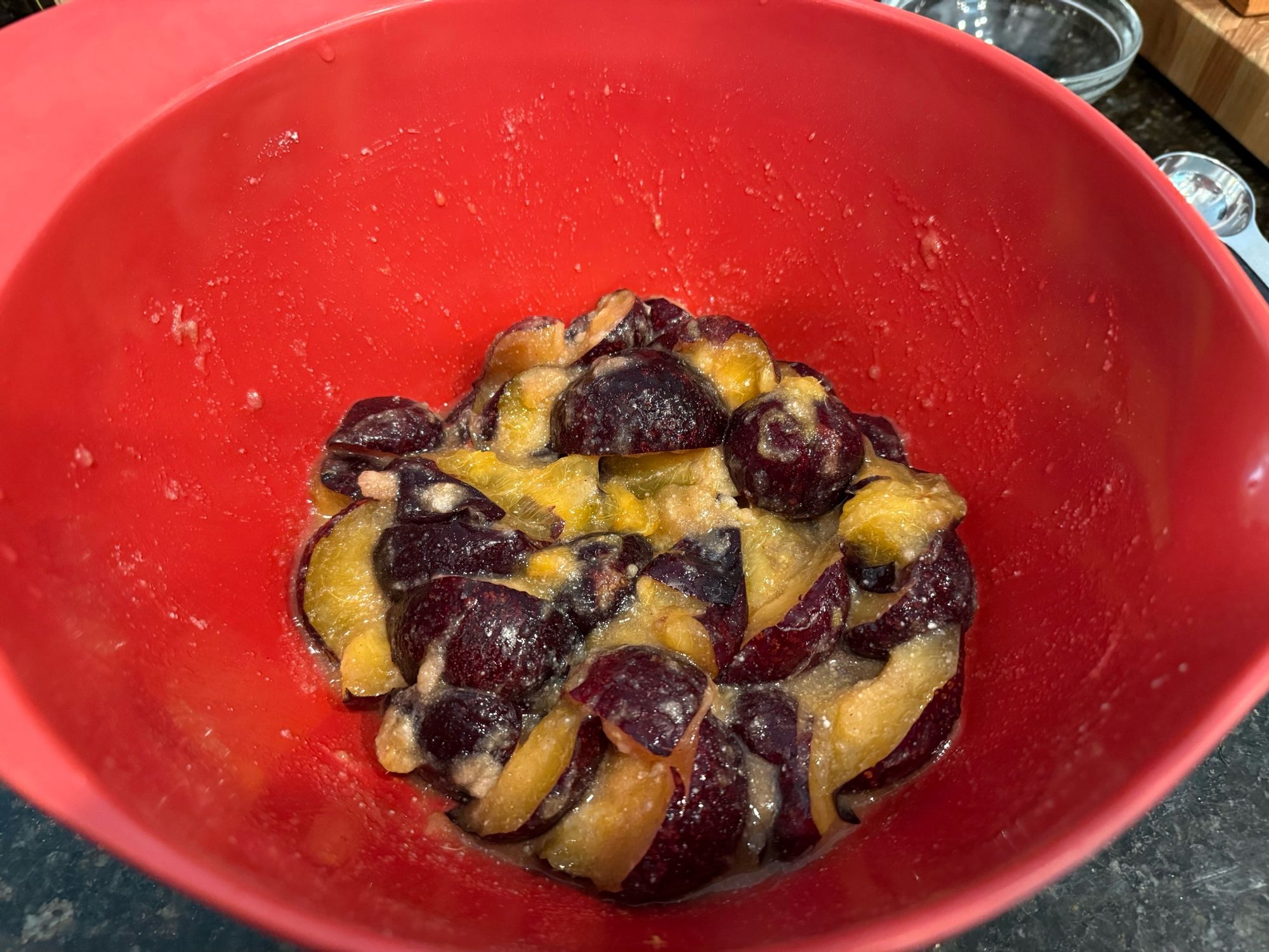 A bowl of quartered plums mixed with sugar, a bit of tapioca starch, cinnamon, lemon juice and zest, bourbon, and a bit of salt. 