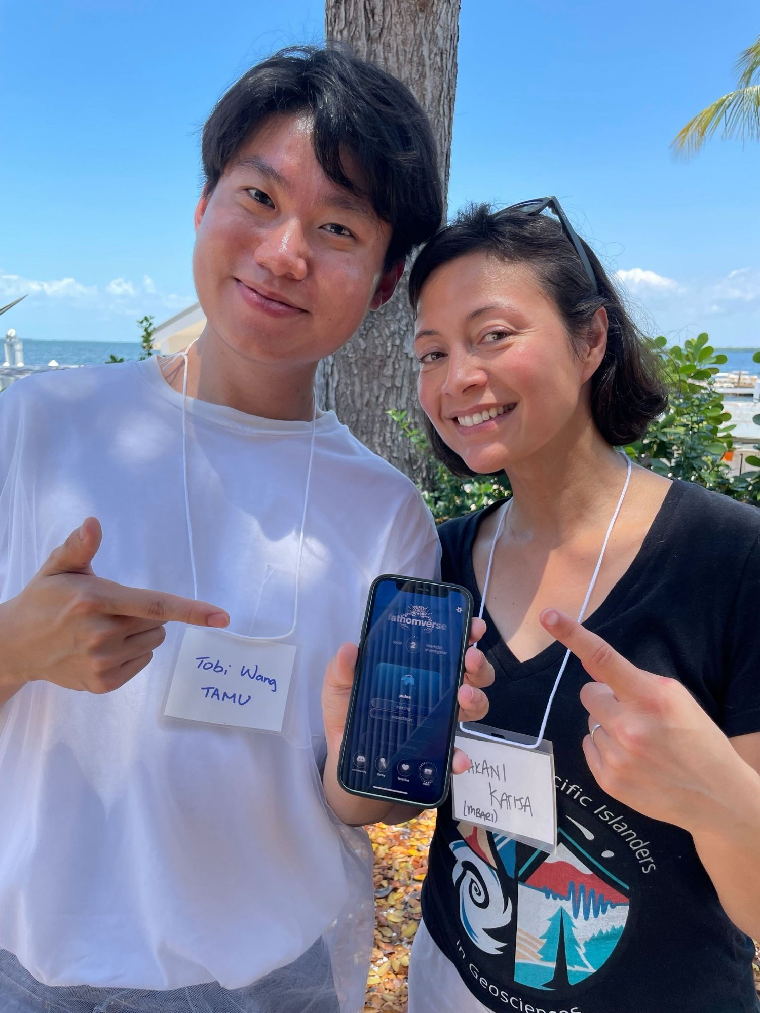 Kakani and Tobi pointing at Tobi’s phone showing his progress in FathomVerse, a game where players contribute to science.