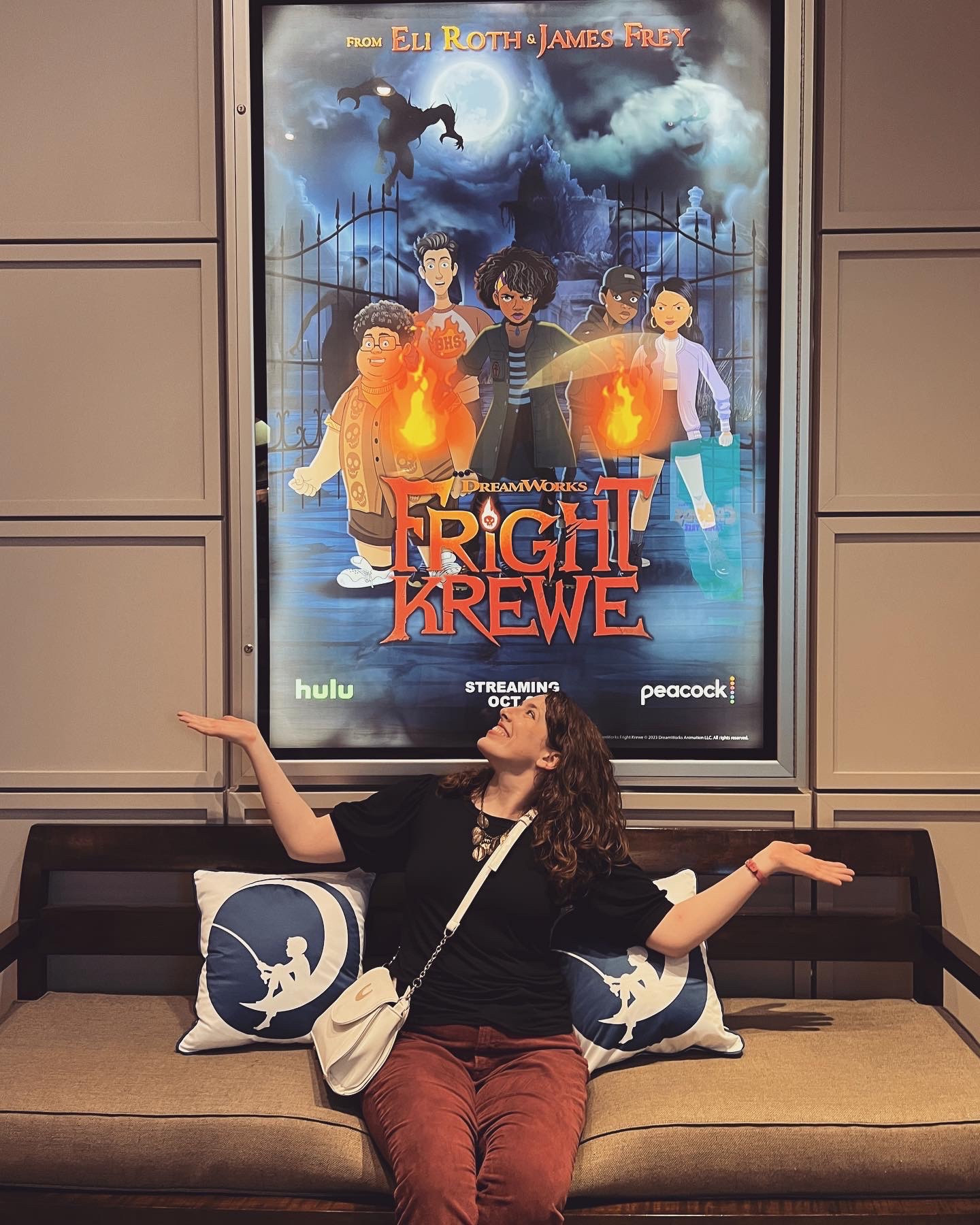 Me sitting on a couch between two Dreamworks cushions beneath a “Fright Krewe” poster