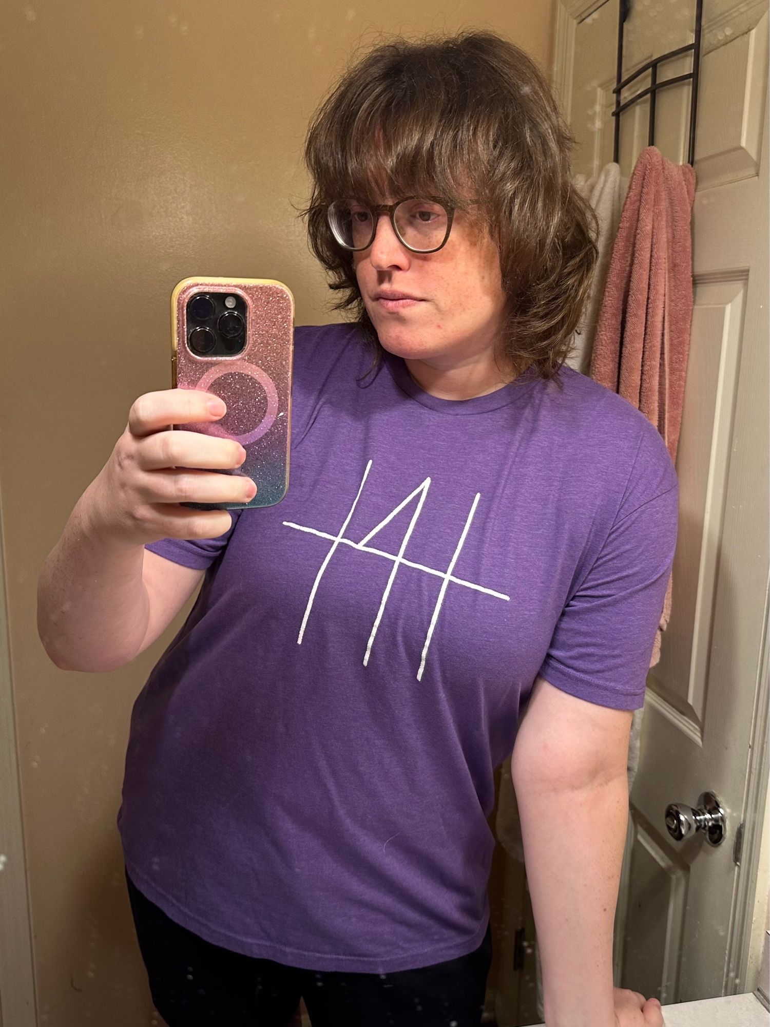 A mirror selfie of Emma. Her hair is messy. She’s wearing a t-shirt that reads “t4t”