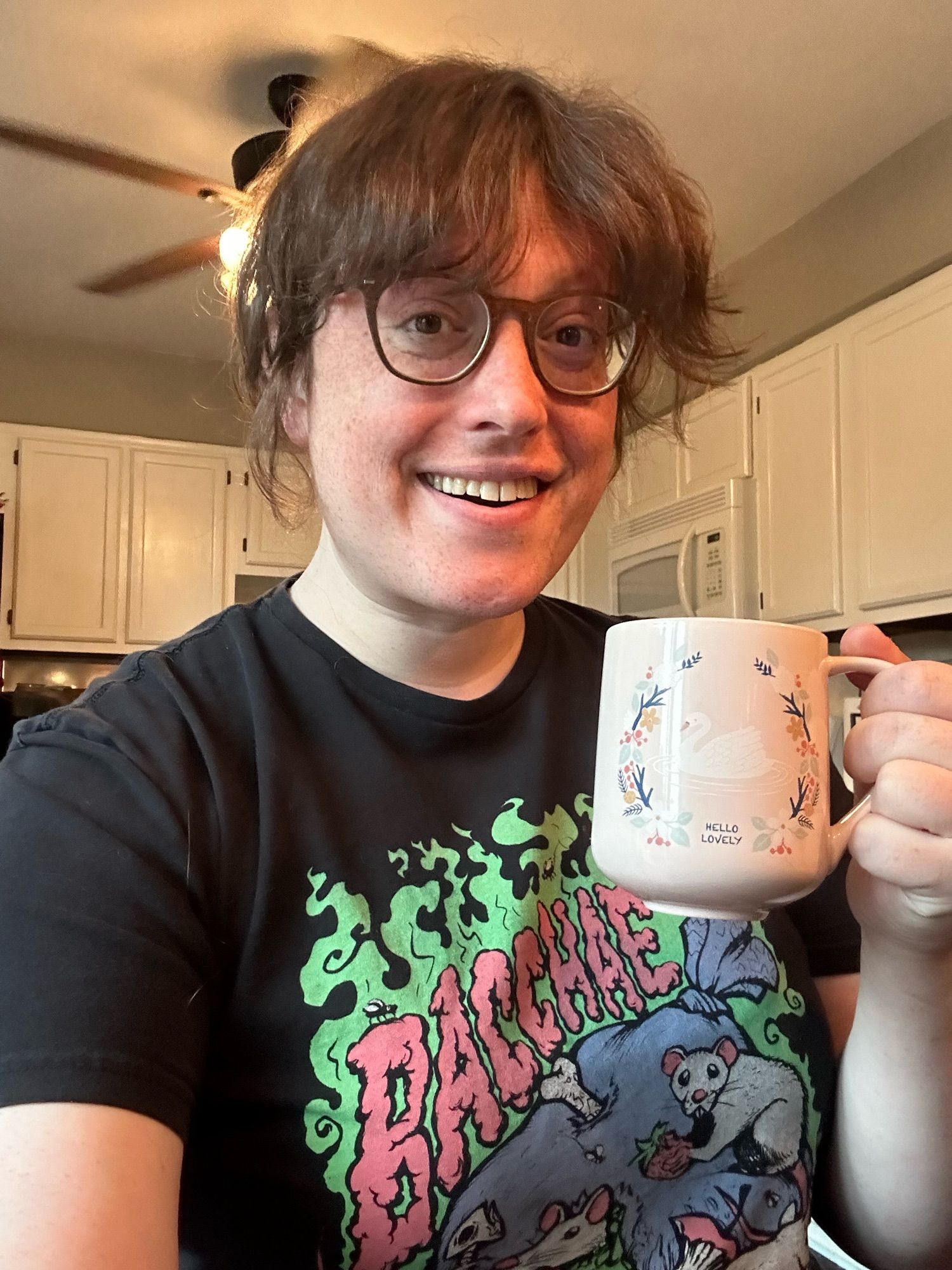 A selfie of Emma. Her hair is up and she’s holding a cup of coffee. Her smile is insincere.