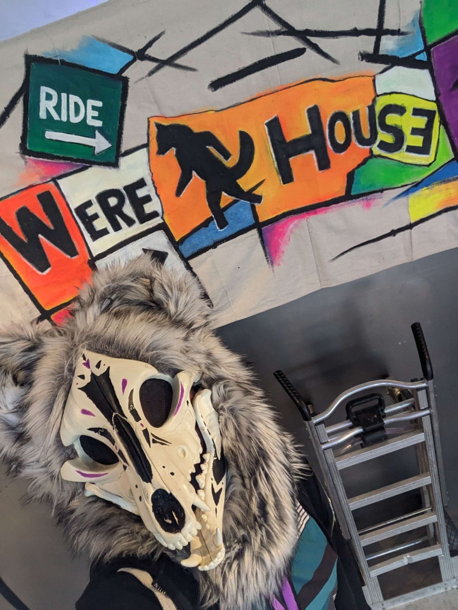 Skull coyote with black and purple markings in front of a brightly colored sign reading Werehouse