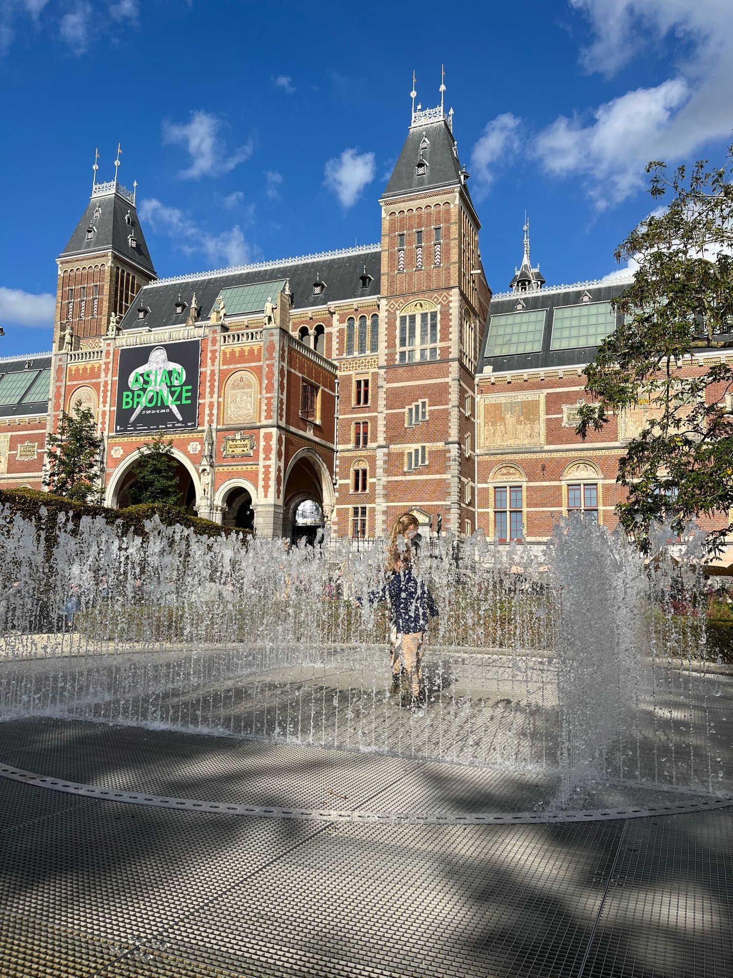 Een fontein met 2 kindjes erin. Op de achtergrond zie je de torens van het rijks museum