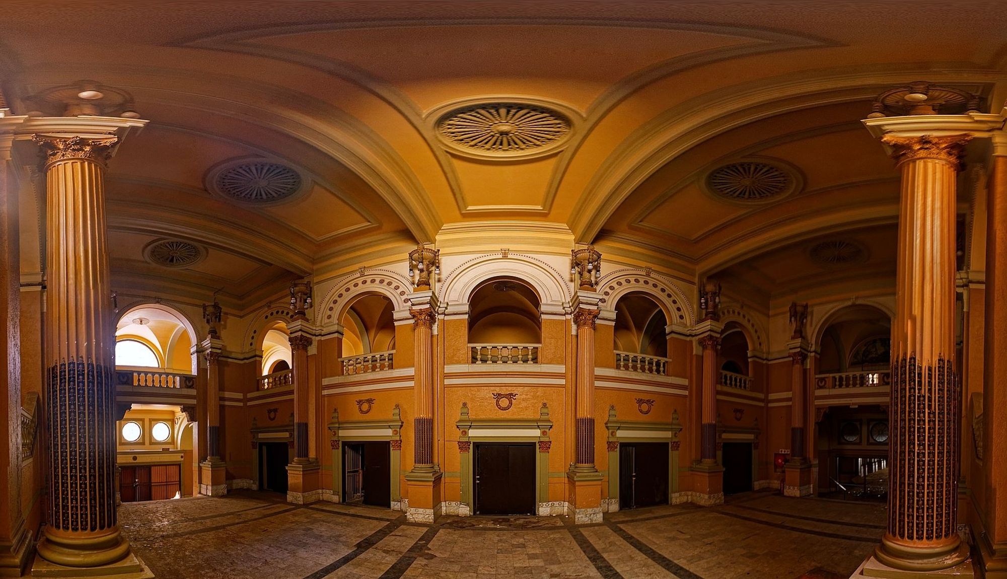 An ornate lobby of an abandoned movie theatre with pillars and arching ceiling.