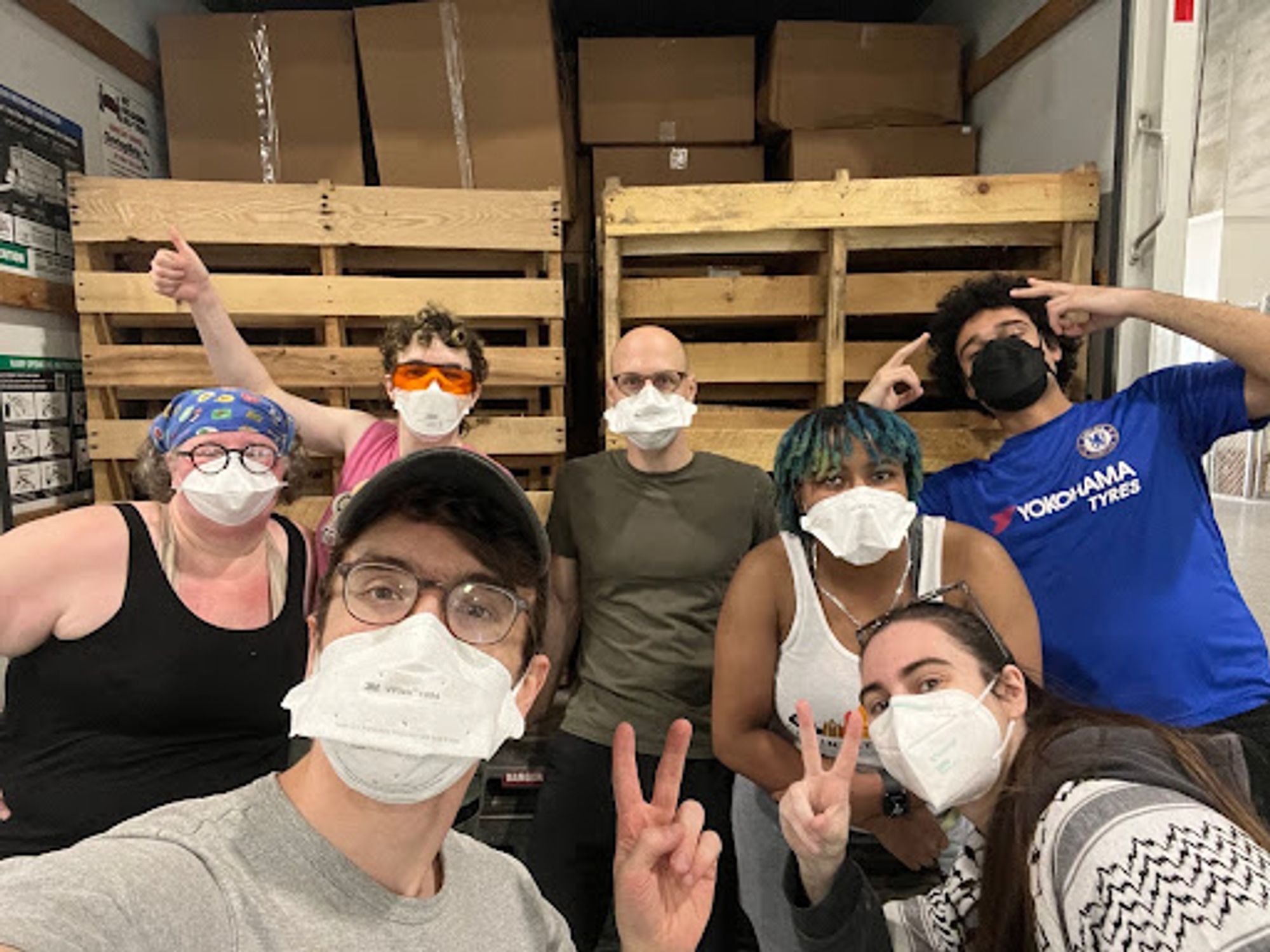 7 people from Maskbloc STL, Maskbloc LEX, Maskbloc Cincinnati, and Louisville take a selfie in front of a uhaul packed with boxes of masks and pallets. They are all wearing masks.