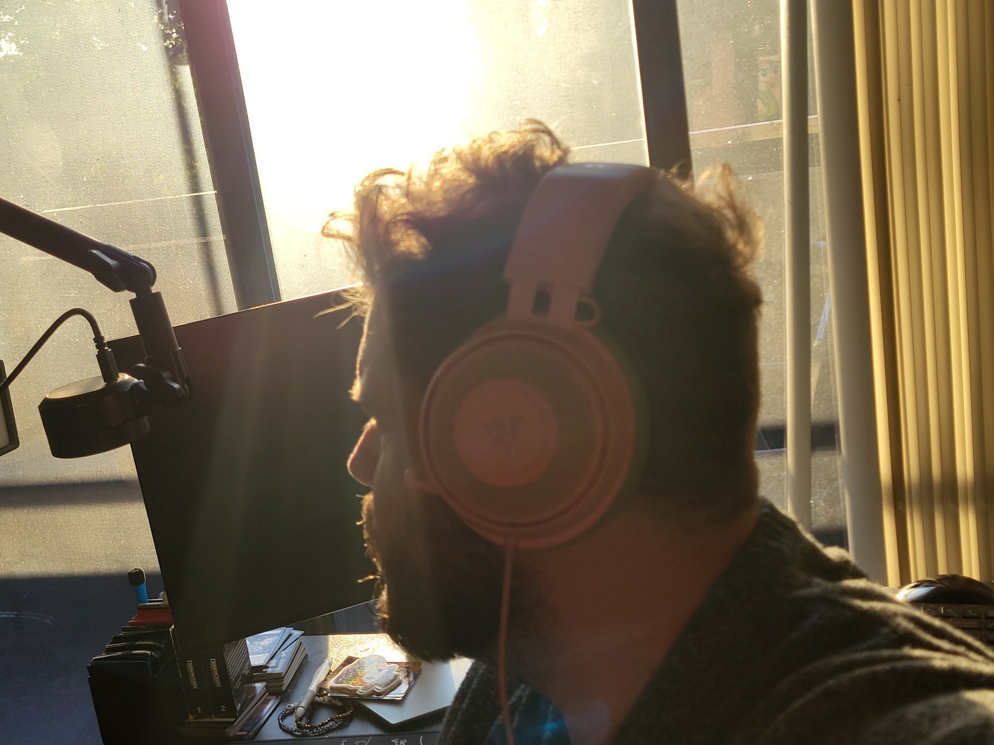 Benji is looking outside from his desk while wearing headphones during the sunset.