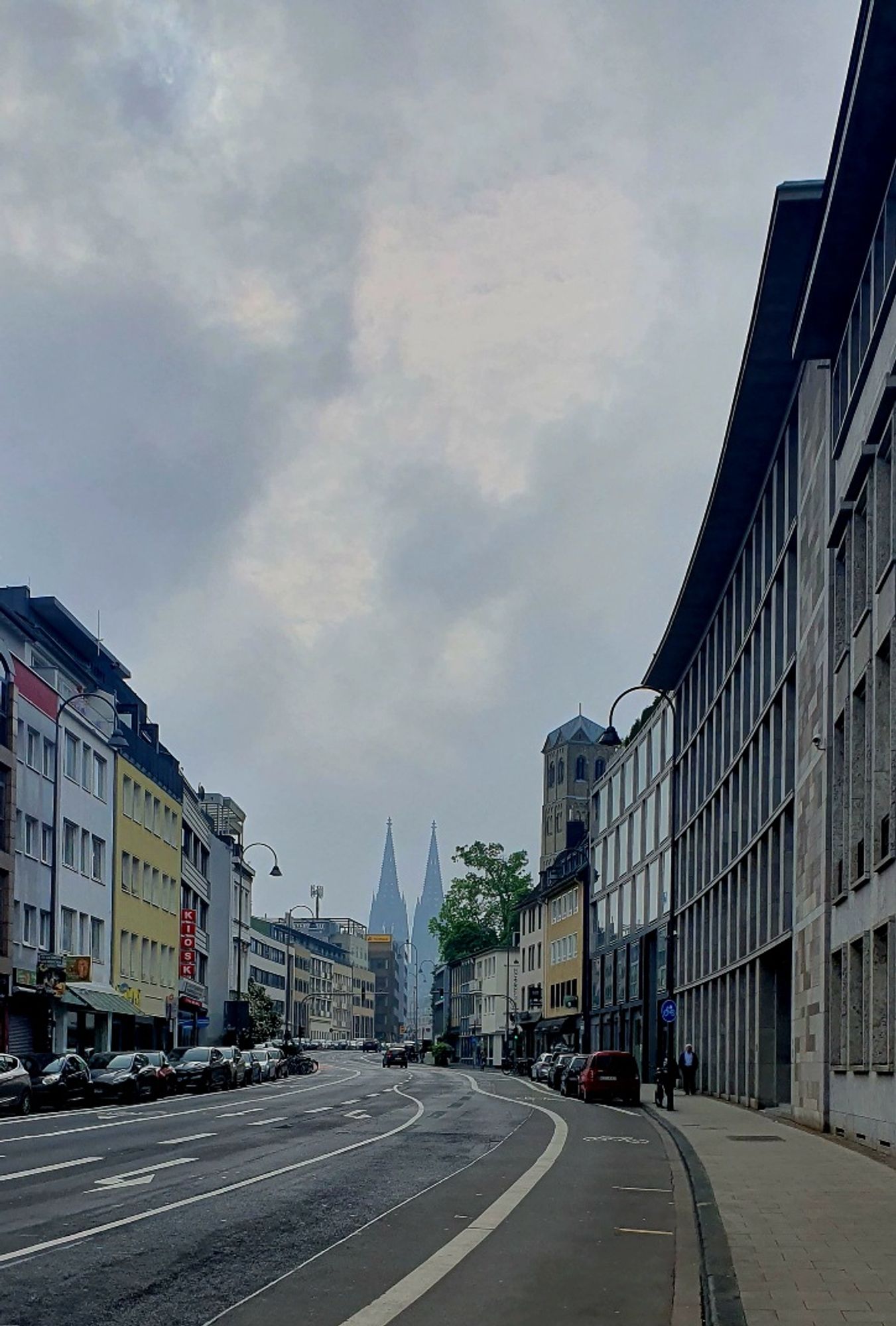 Leere Strasse mit parkenden Autos, am Horizont ein Dom