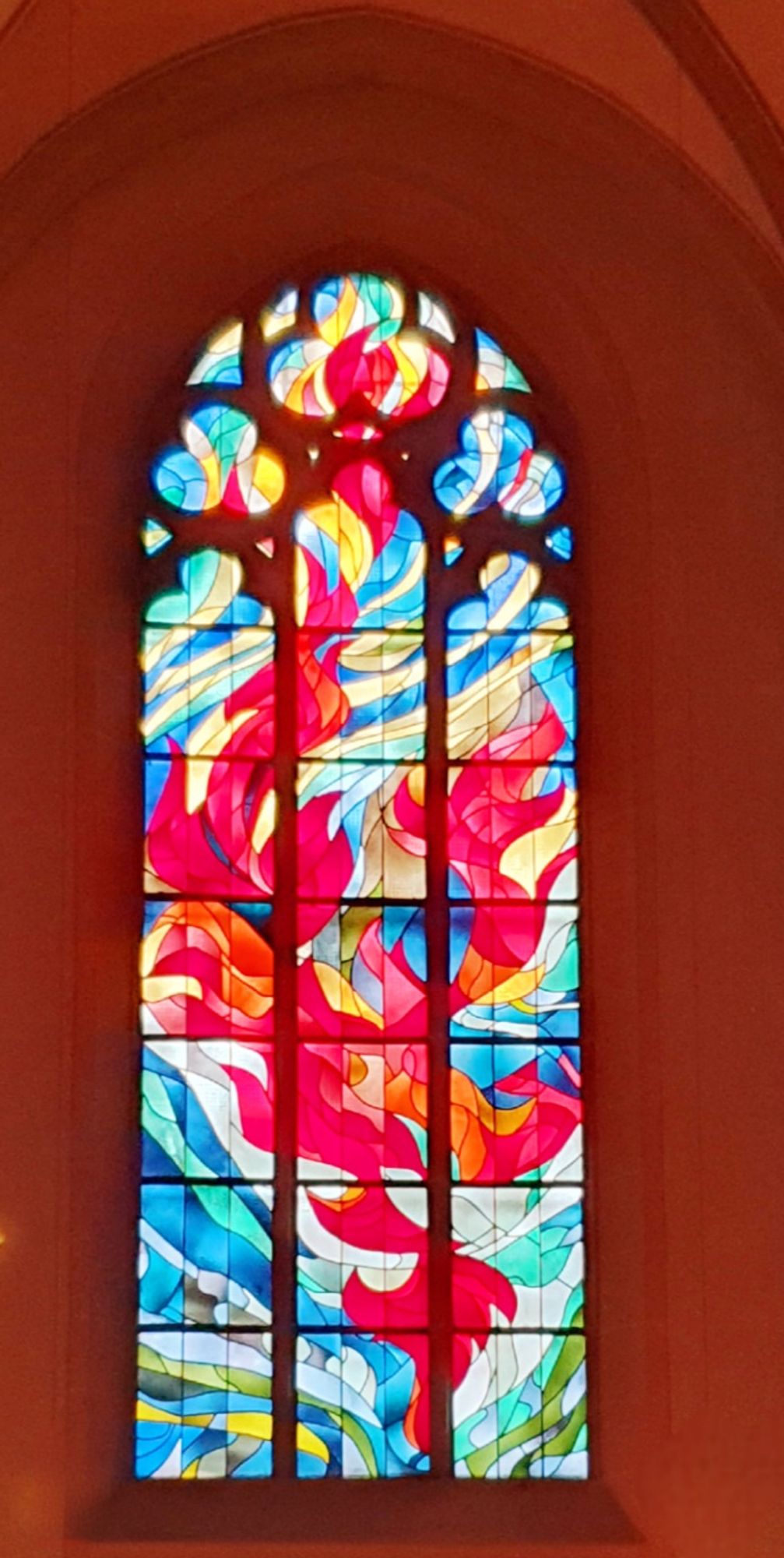 Ein Kirchenfenster, blaue verschlungene Linien und eine rote Flamme