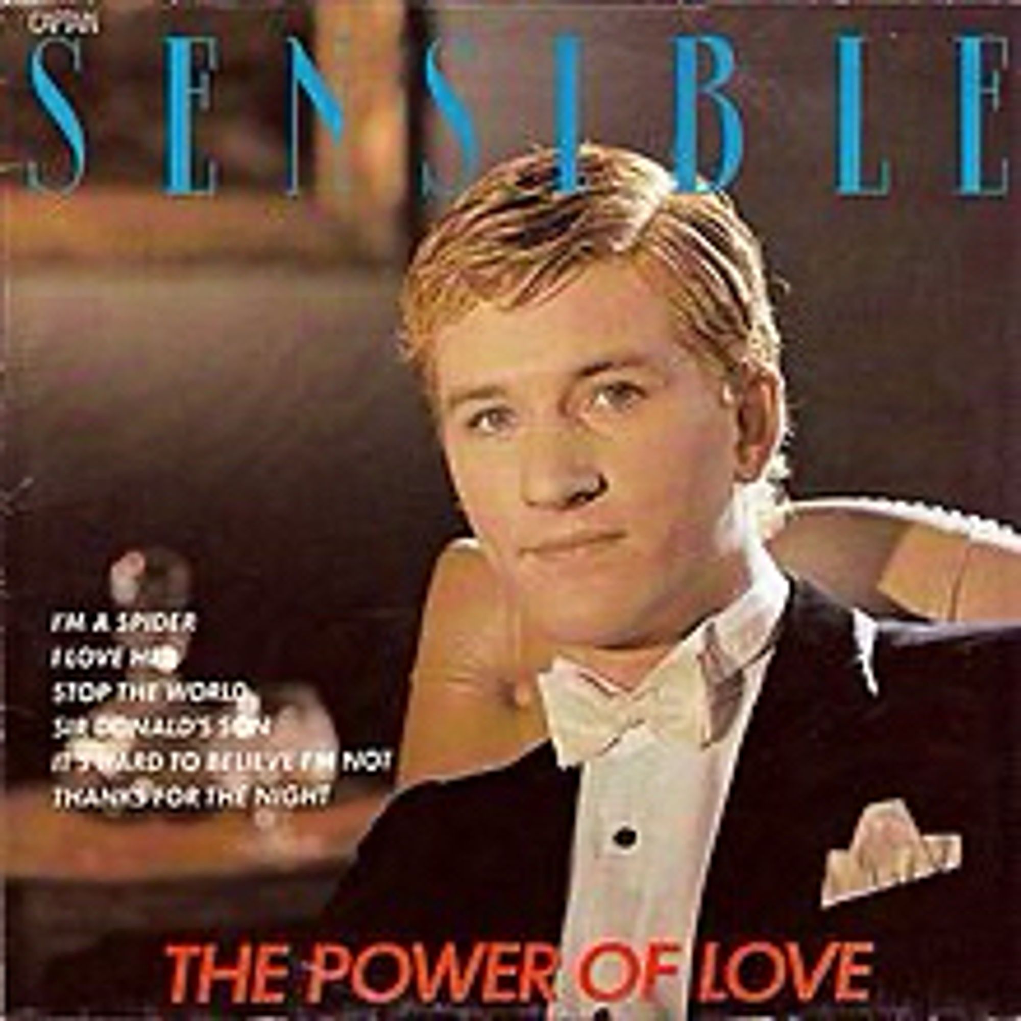 The cover of The Power of Love, the second solo album by The Damned guitarist Captain Sensible. The Captain is sitting in a posh hotel room or library. There’s no sign of his trademark beret and shades but at least he has his kit on. He’s wearing a tuxedo with a winged collar and white bow tie. Did he go to Eton? Would explain his swift promotion from midshipman. He sits in a cream leather chair, a decanter and a framed picture in the background. Always decant your snakebite and black.