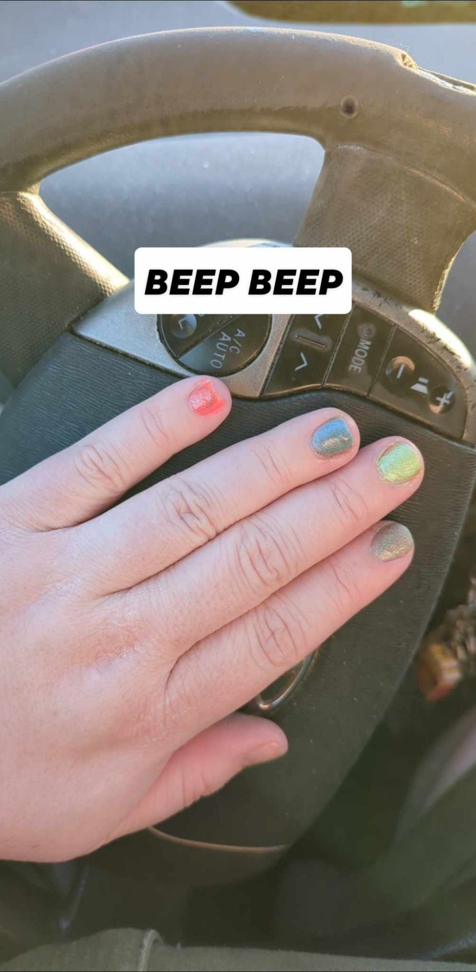 A white hand with painted nails;  one orange, one blue, one green, and one grey. They all sparkle. The hand is pressing on a car horn and the text reads "beep beep"