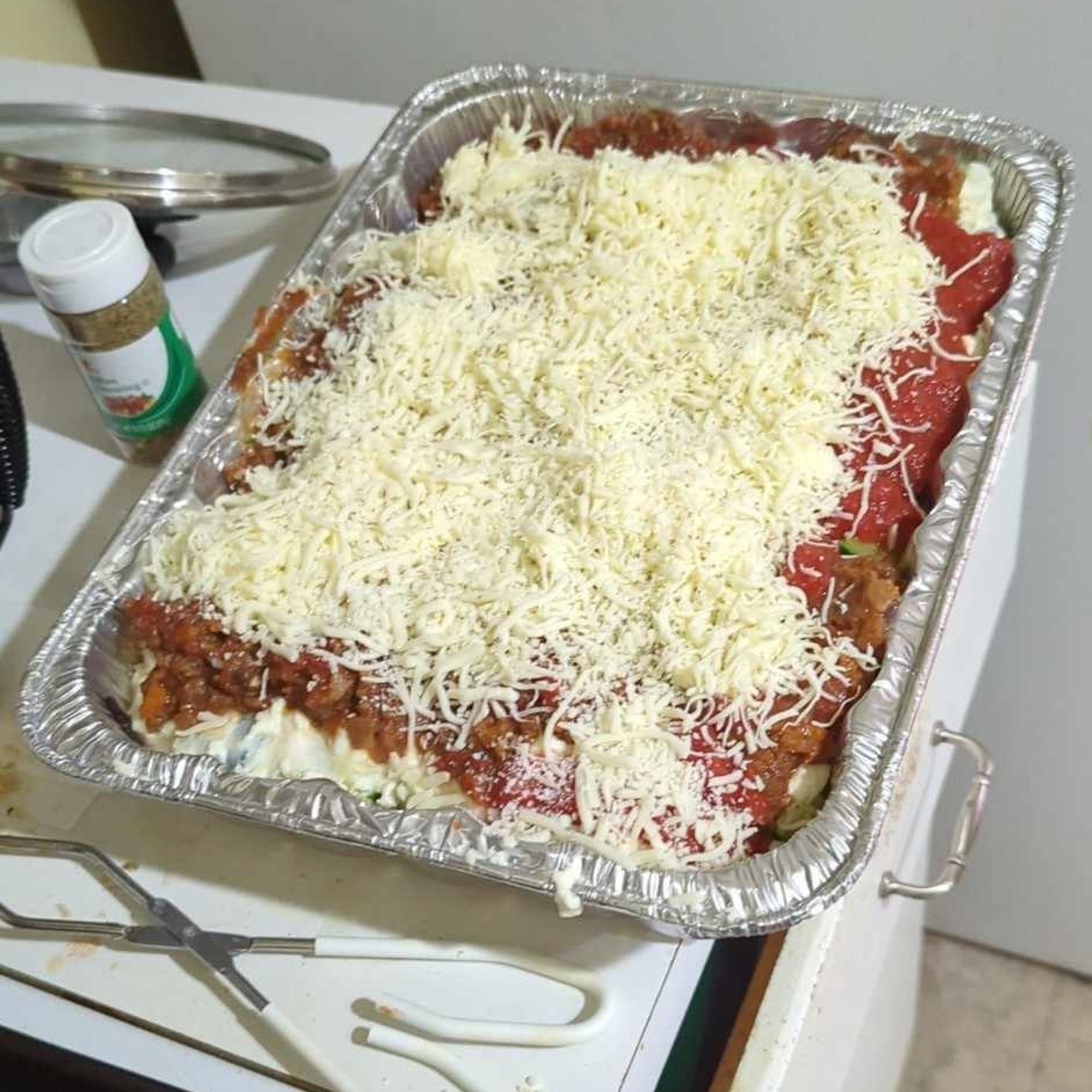 A nearly over flowing lasagna pan with a big pile of shredded mozzarella on top