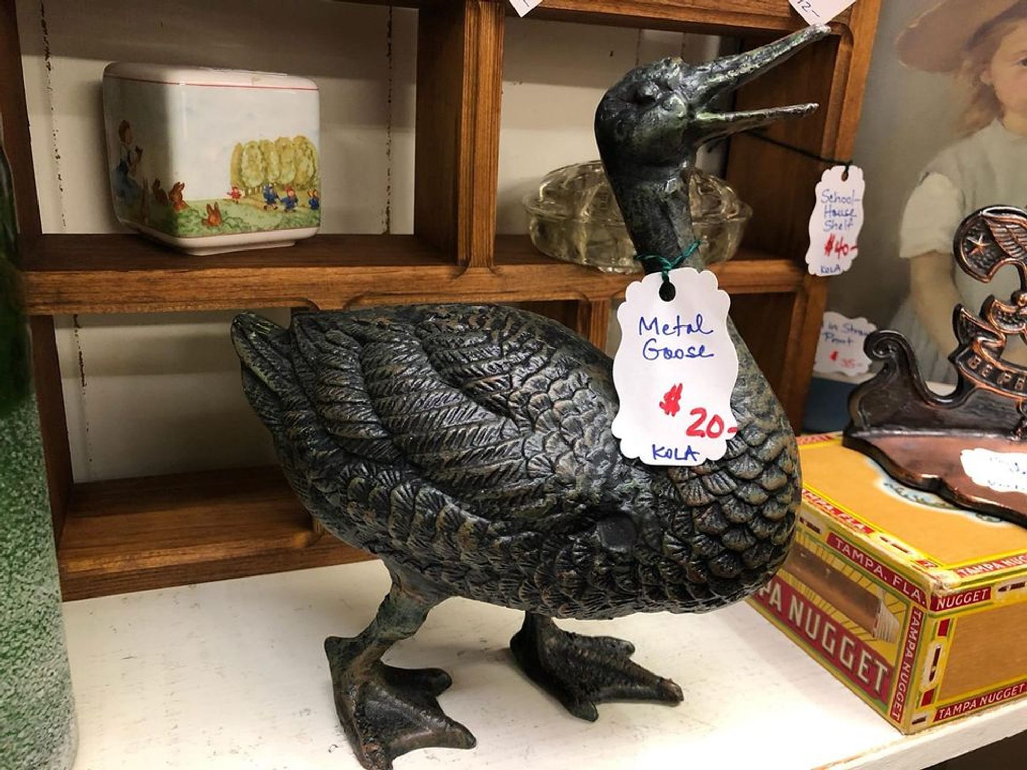 a black metallic goose statue, a tag hangs from her neck saying "metal goose $20 kola"