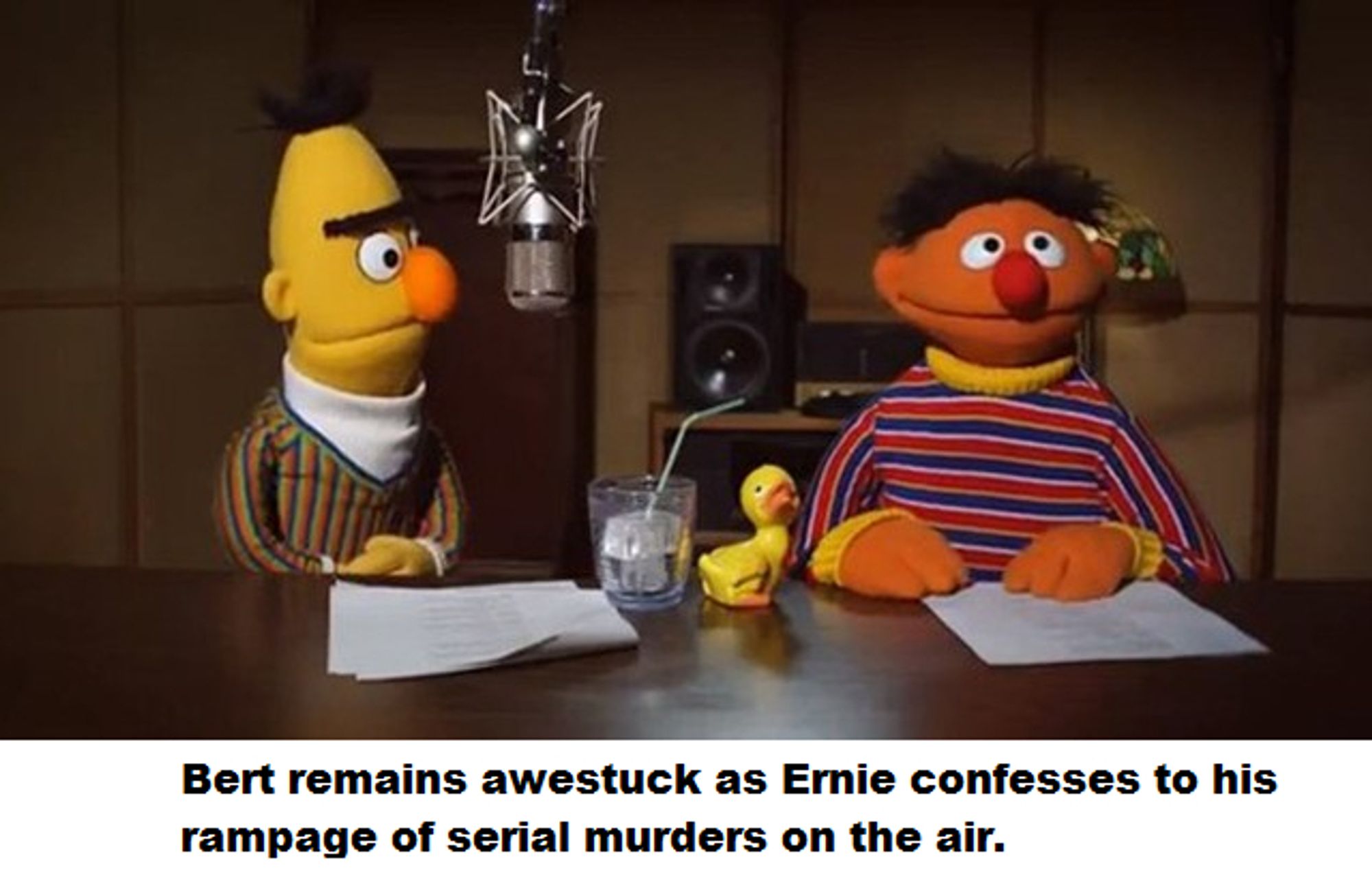 Burt and Ernie sitting behind a microphone.  Burt is looking at Ernie, looking slightly offput.  Ernie is looking slightly off camera, but mostly towards the viewer.

The text at the bottom: "Bert remains awestruck as Ernie confesses to his rampage of serial murders on the air."