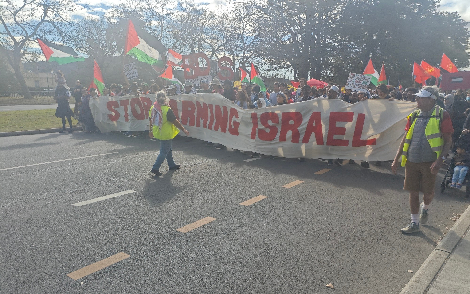 A picture from the front of the rally in Canberra today. Many Palestinian flags and a banner is being carried saying "stop arming israel". Also a few marshals in high vis are visible 