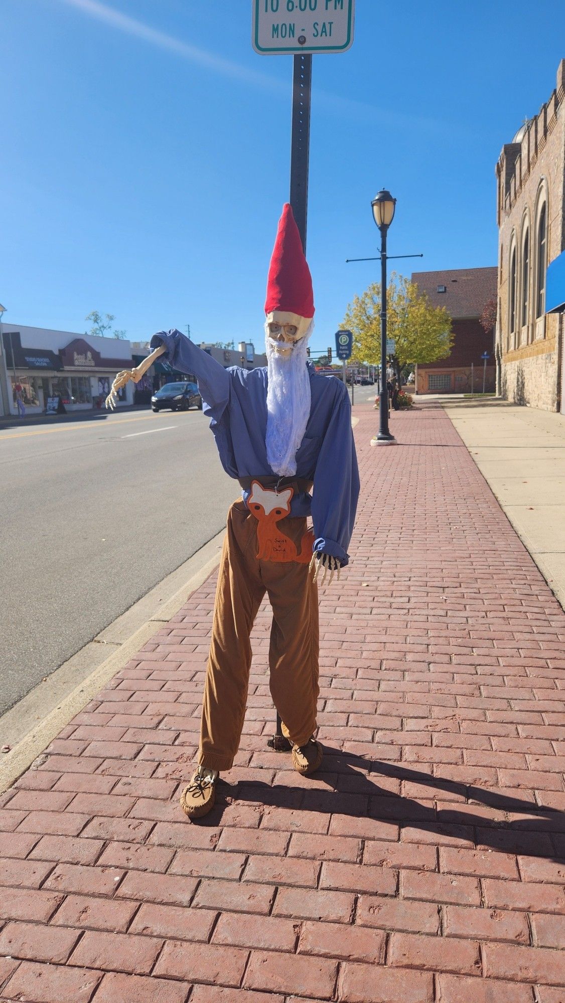 A replica skeleton dressed with a red cone-shaped hat, long white beard, blue shirt and brown pants, to resemble a garden gnome.