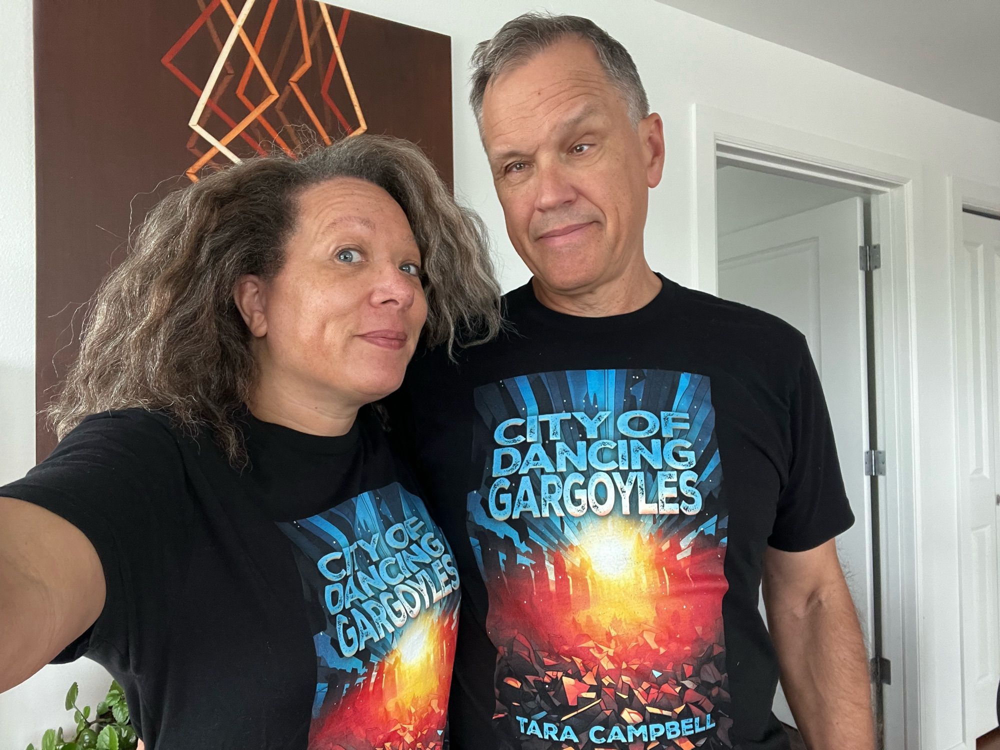 Man and woman wearing black T-shirts with the blue, orange, and yellow cover of the novel CITY OF DANCING GARGOYLES