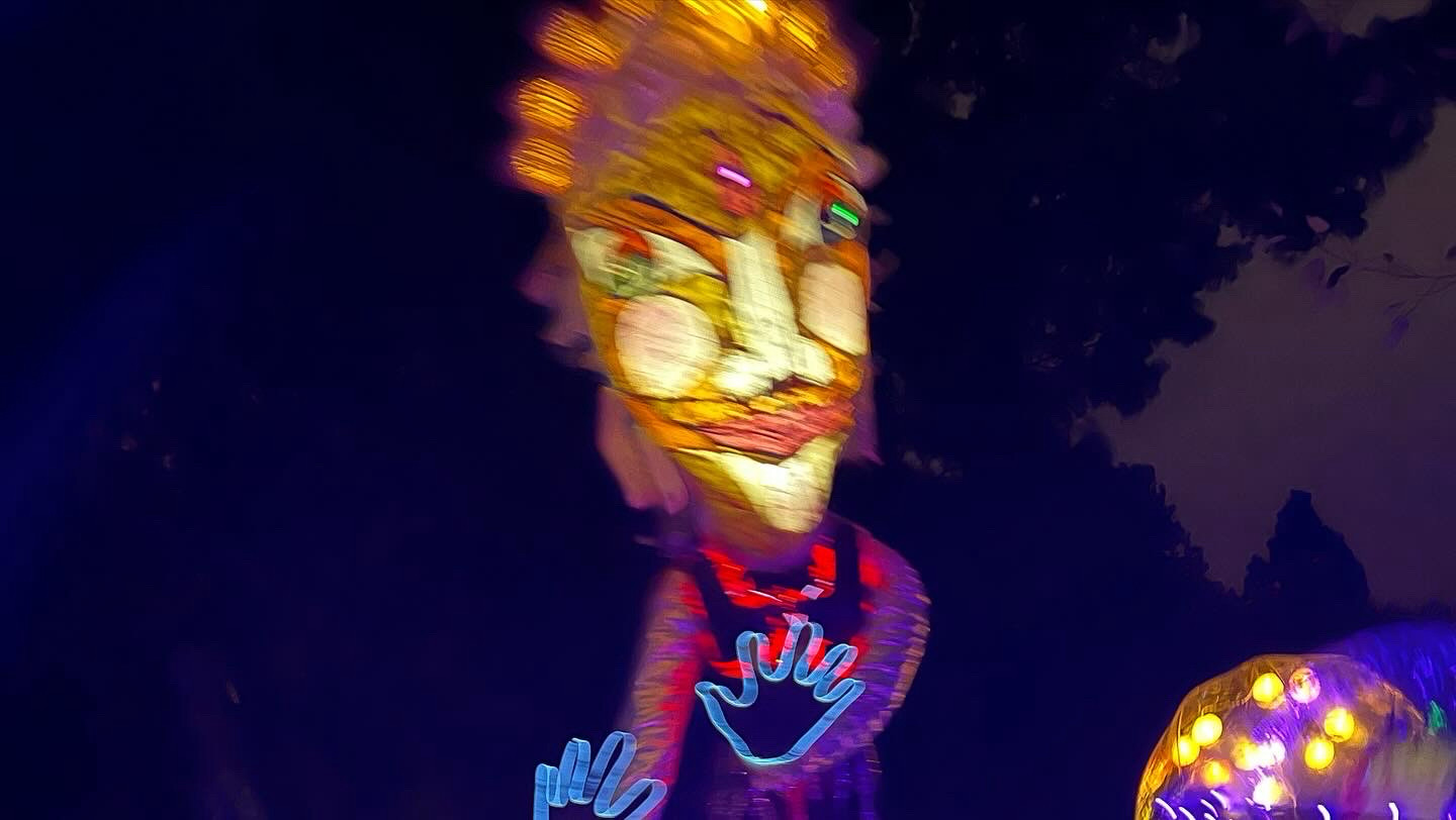 A larger-than-life lantern shaped like a woman with green eyes and orange hair. Hands are outlined with glow sticks.