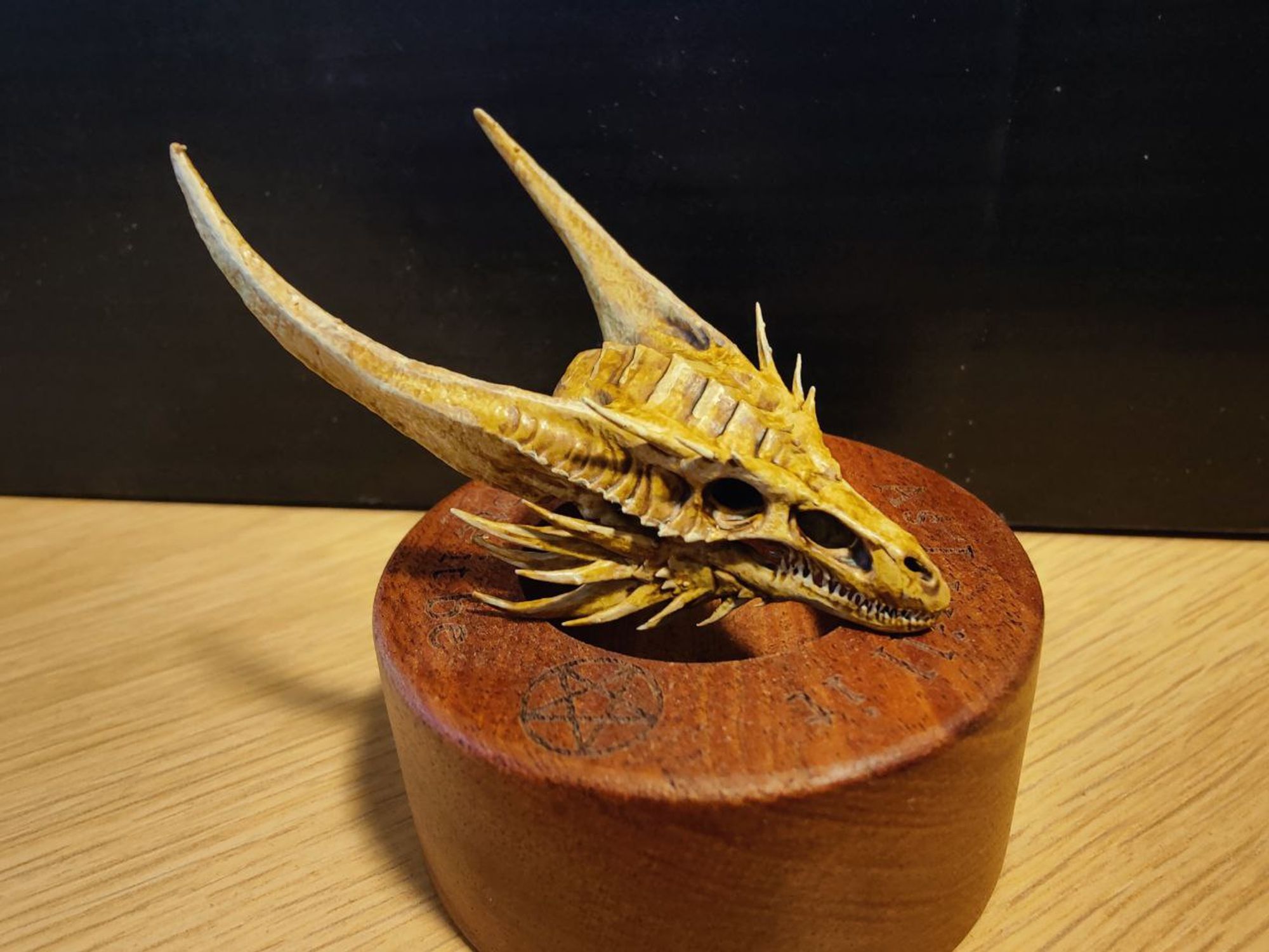 3D resin print of the skull of the dragon Sunfyre from House of the Dragon, painted and displayed on a wooden cylindrical block.