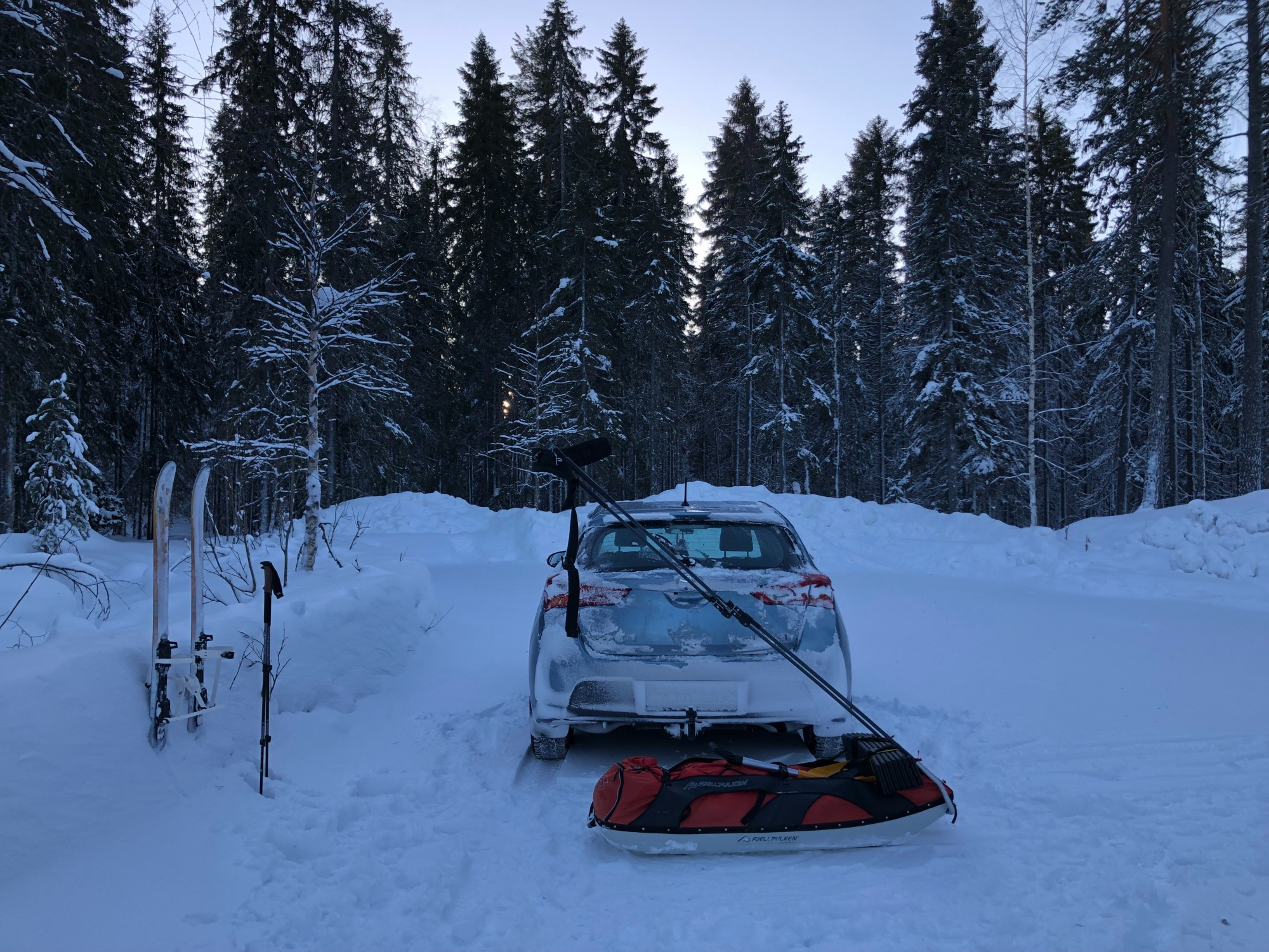 A small Toyota with a large pulk in the northern boreal forest parking spot. My skis and poles in the snow.