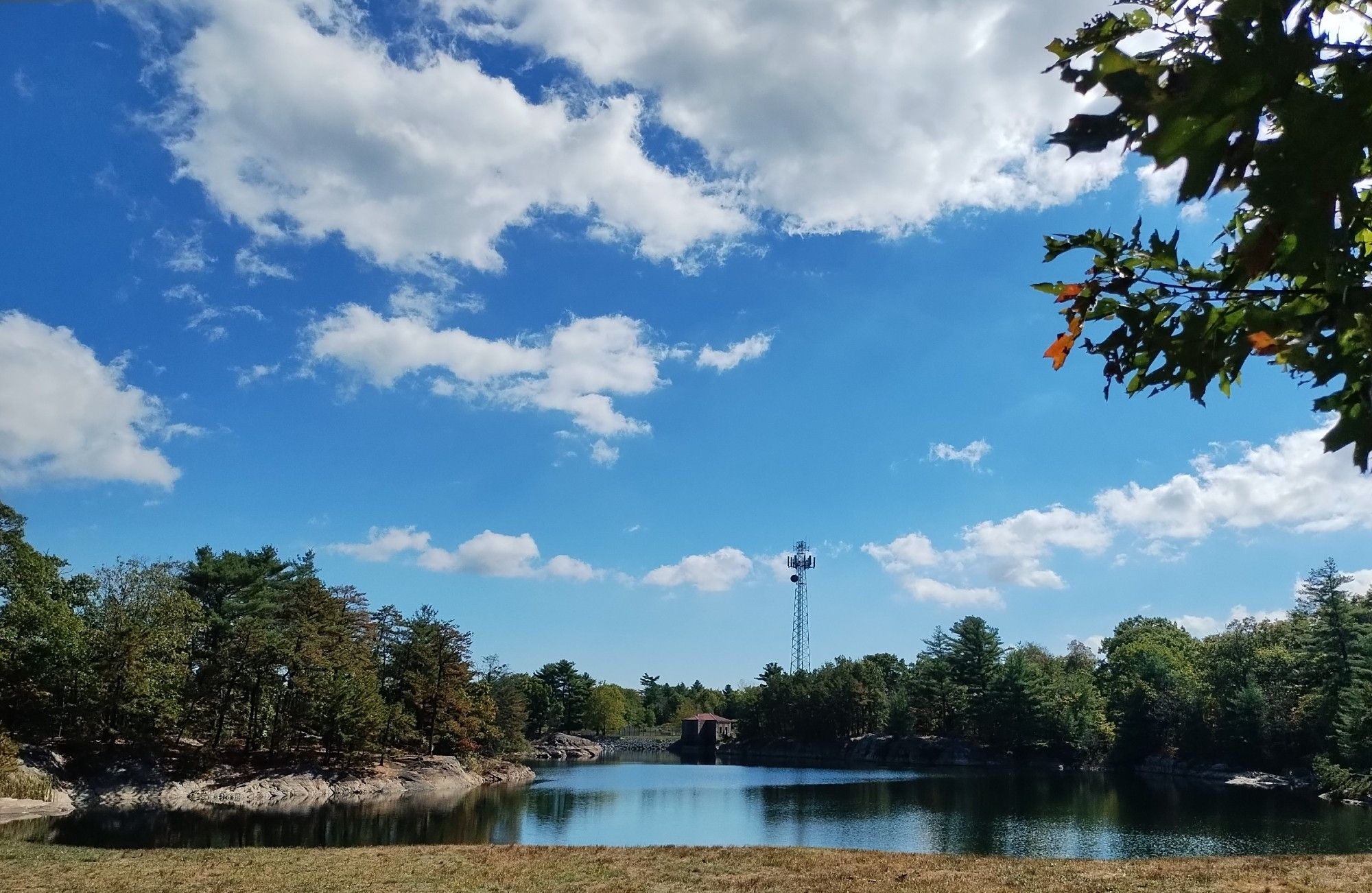 photo: blue sky over a little reservoir lined with granite and oak trees, a small cell tower on the far bank