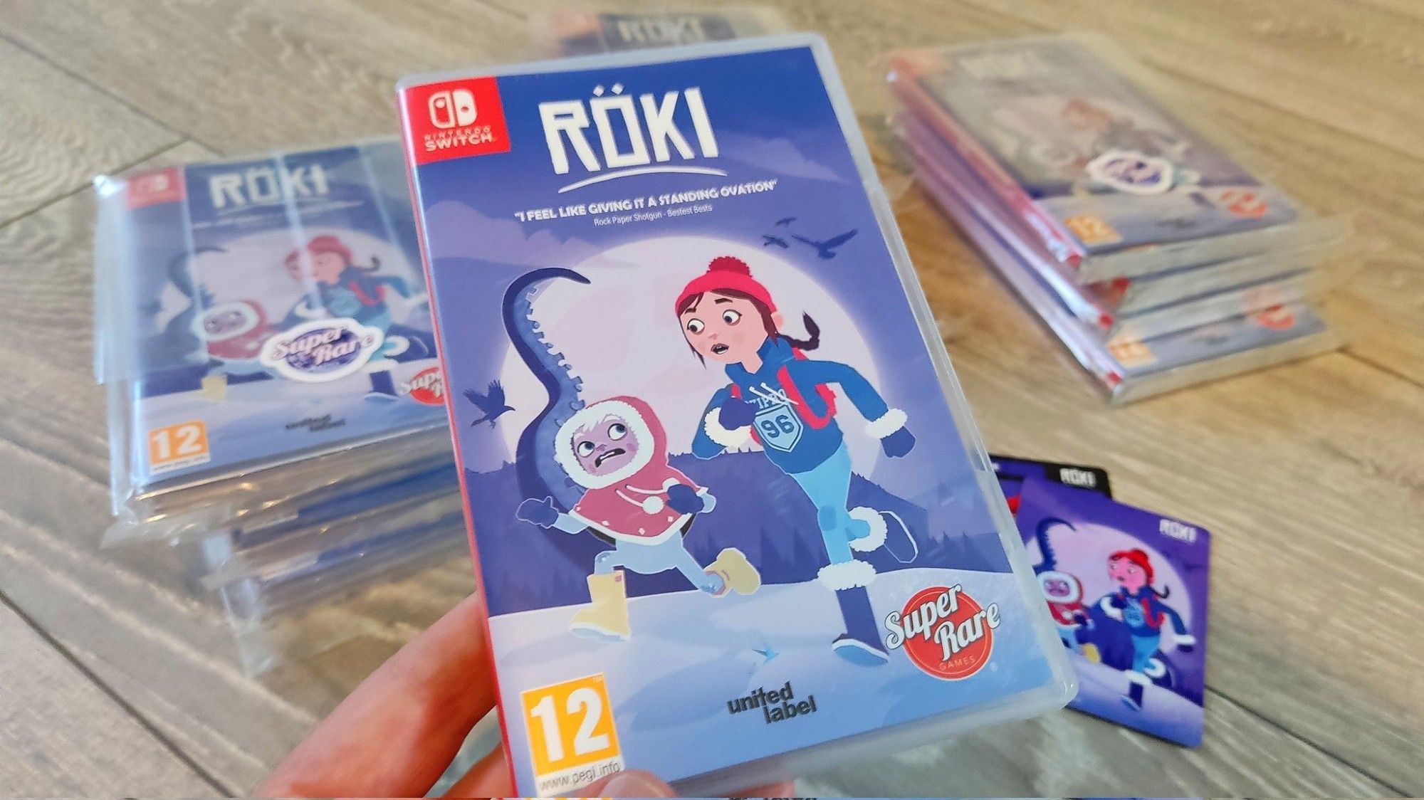 Me holding a physical copy of the indie game Röki with some other copies in the background