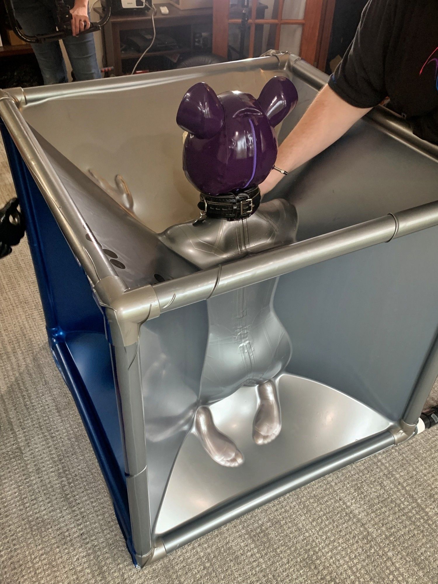 Kneeling inside a vac cube wearing inflatable cat hood, backside