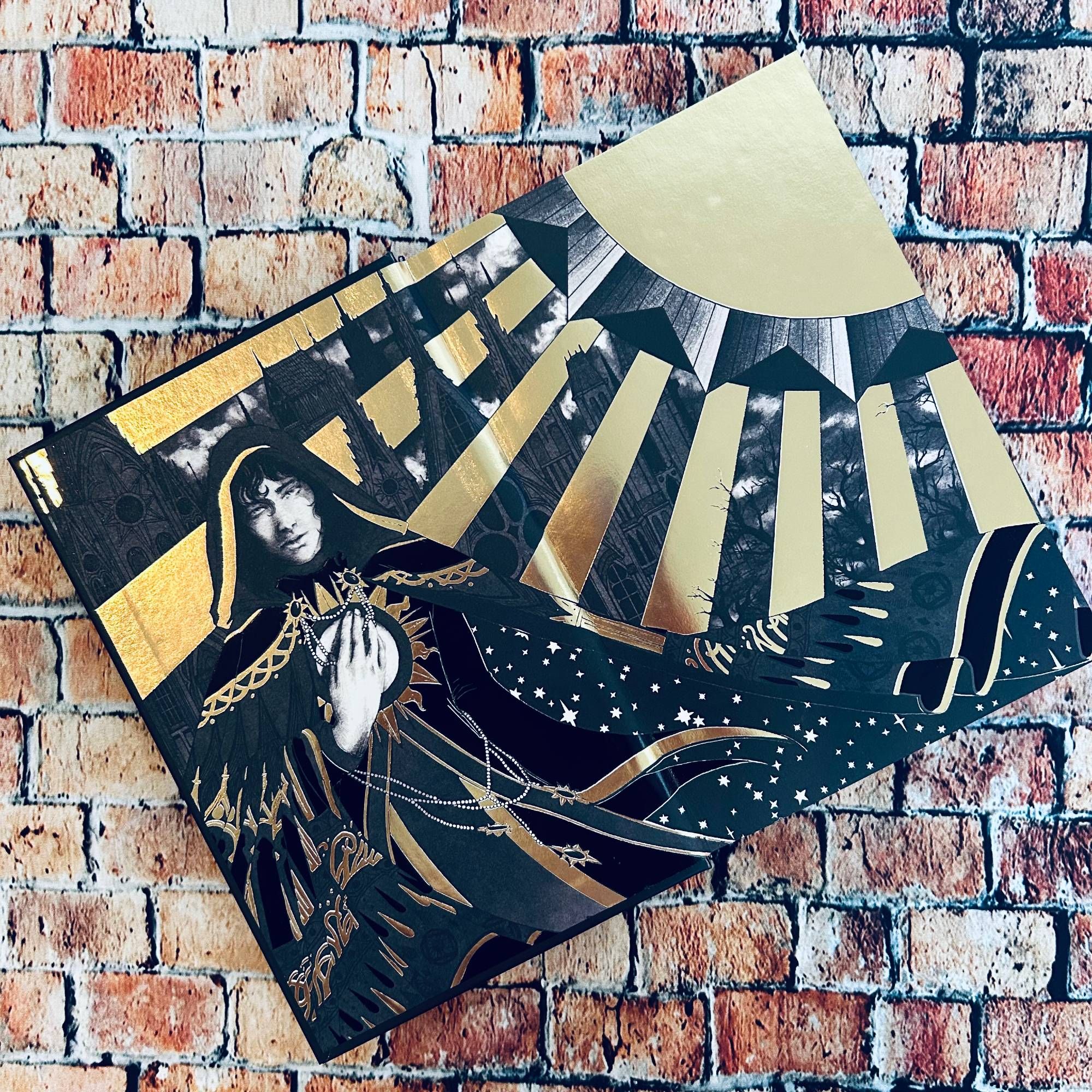 Close up of the front endpapers of Ilya in his priest robes under the sun; the illustration is black and white with gold foiling.