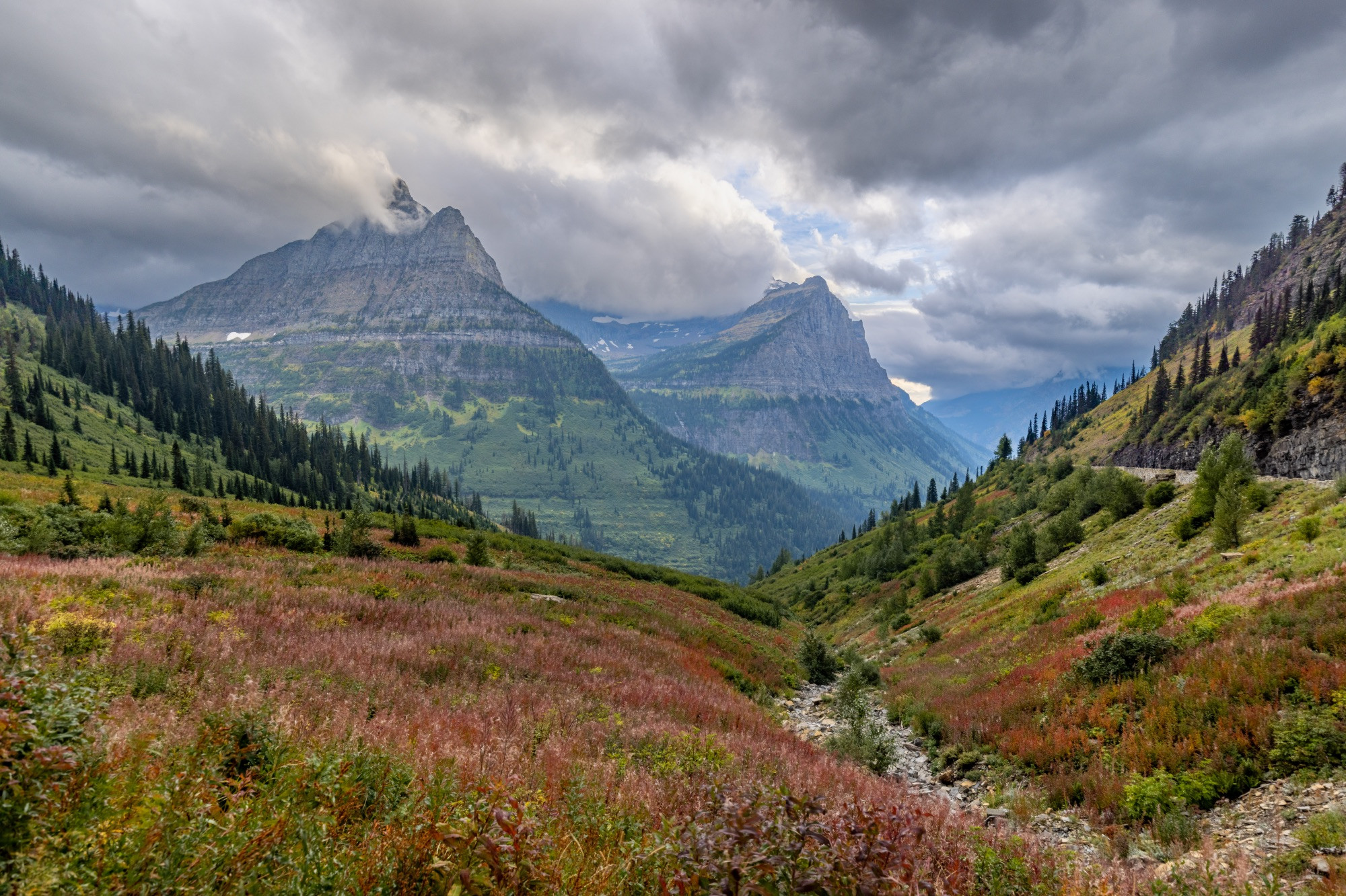 Big bend overlook at Glacier National Park. Colorful mountain scenery fills the foreground with two huge peeks filling the middle ground. The skies are cloud and the scene is dramatic.