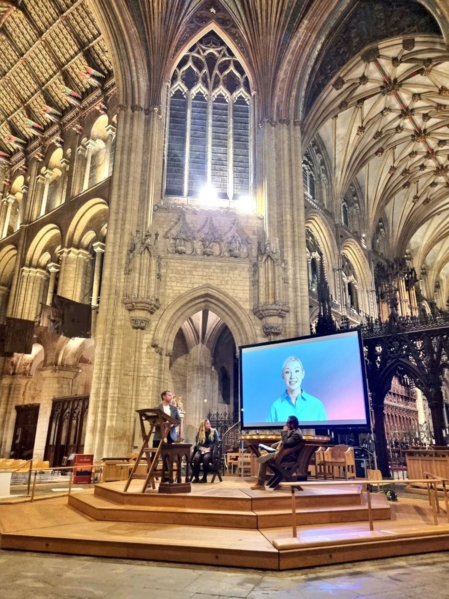 AI-generated woman on a large screen in the centre of Ely Cathedral