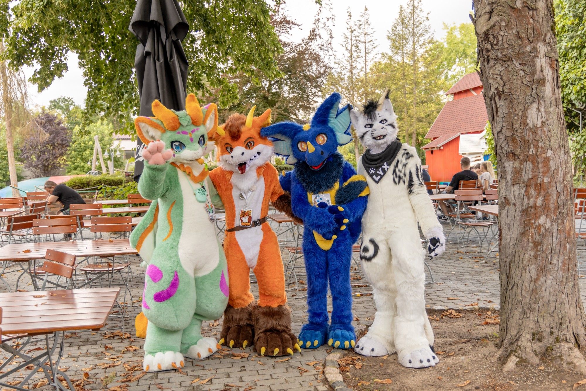 Group photo of 4 dragons, left to right: green dragon with orange horns and a carrot; orange dragon with brown hair; blue dragon with yellow horn on nose; white dragon with black markings