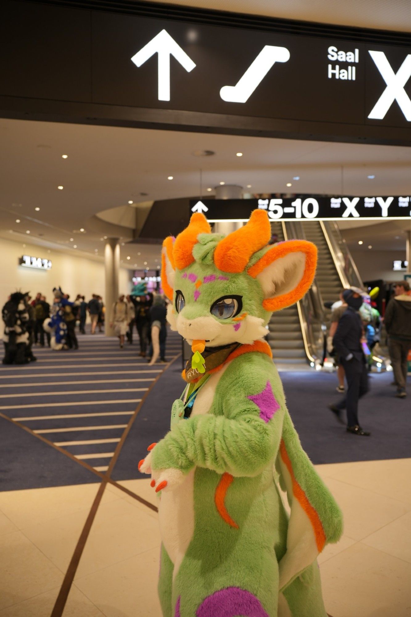 A green dragon with blue eyes and orange horns visiting the Eurofurence 28.