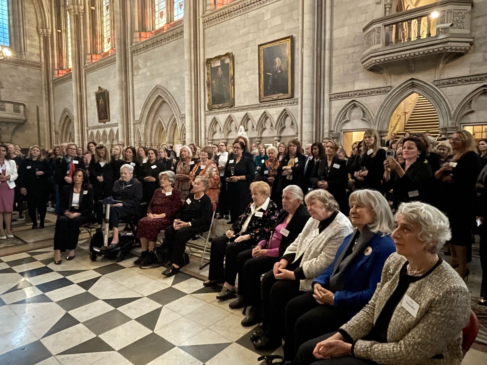 A photograph of women seated and standing listening to a speech inside the Royal Courts of Justice.