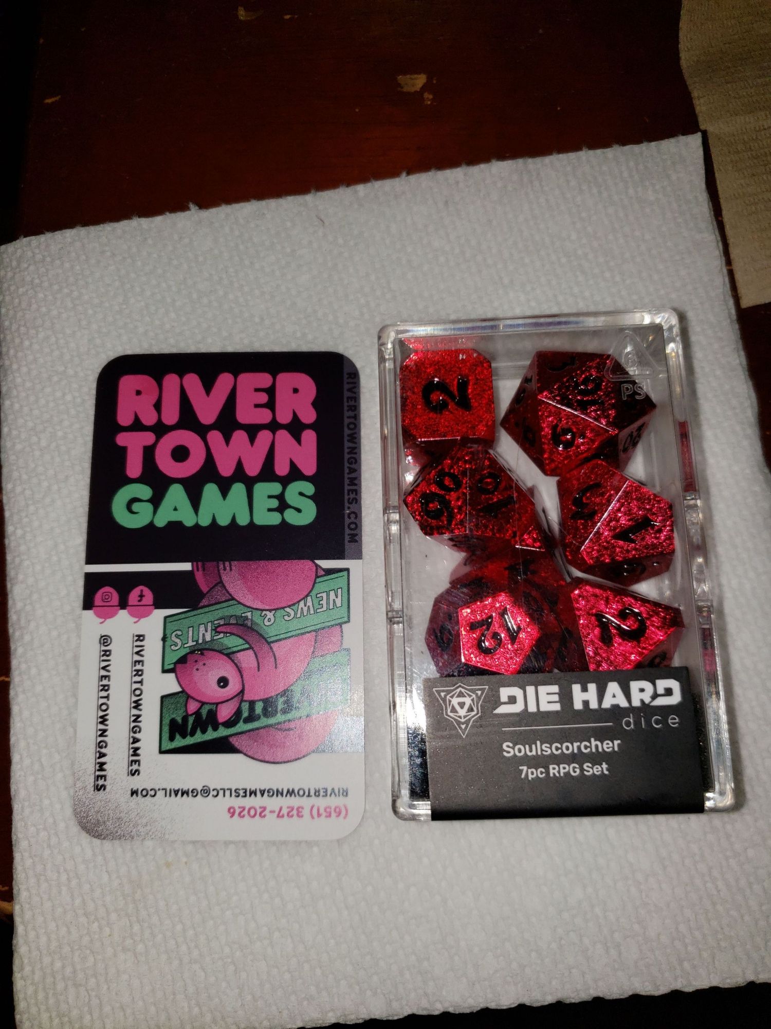 A set of red dice for use in tabletop RPGs next to the business card for the store where the dice were purchased.