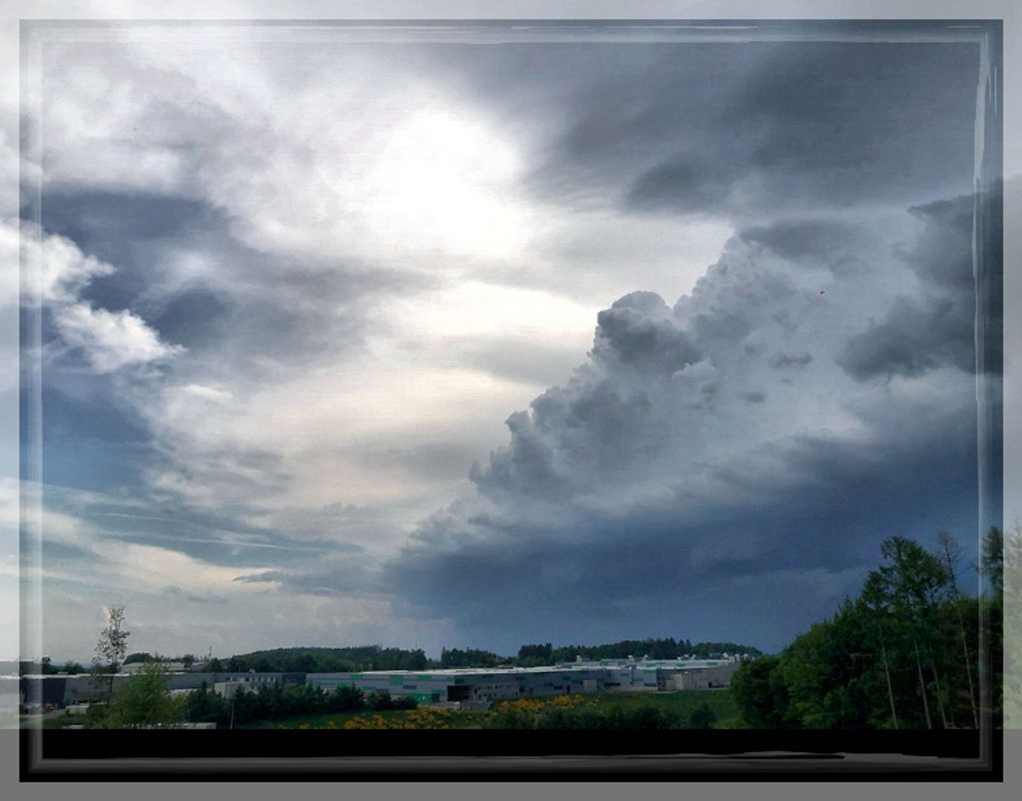 Eine dunkle Wolke, die sich wie eine Welle von rechts ins Bild schiebt. Der Blick geht weit in den dunklen Horizont. Momente vor dem Gewitter.