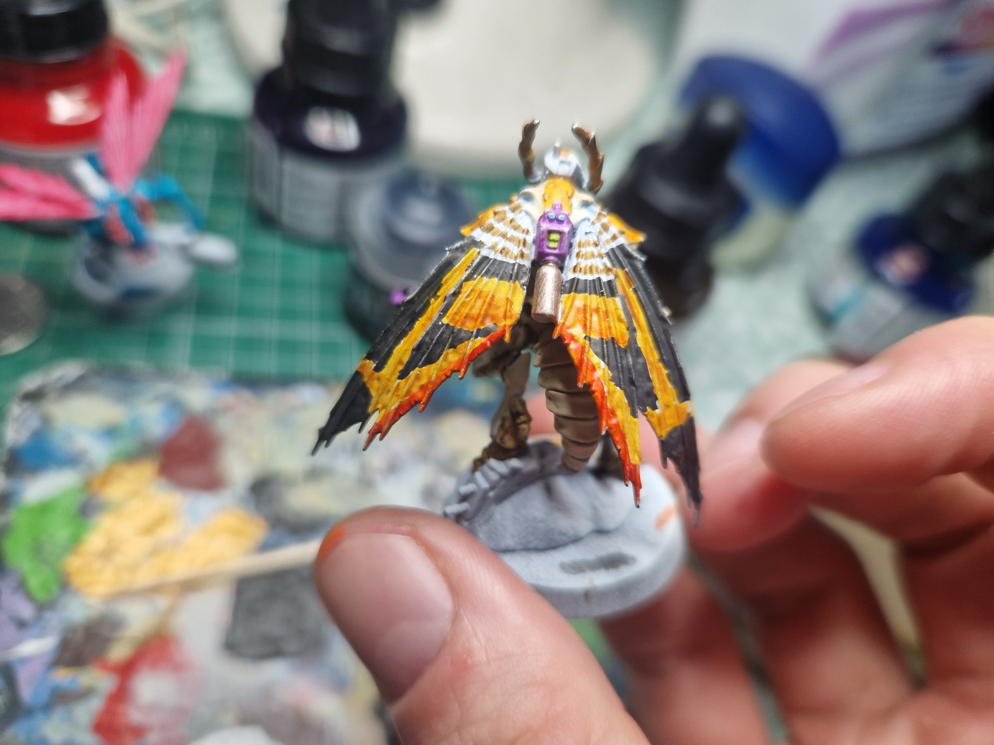 A model of a Vespid (bipedal insectoid warrior with moth wings, a futuristic blaster and a full-face helmet)

The paint scheme is designed to invoke Mothra, with pale limbs, red and orange stripes on black wings and a white helmet with bright blue eye lenses
The view focuses on the red and orange gradient stripe across black wings 