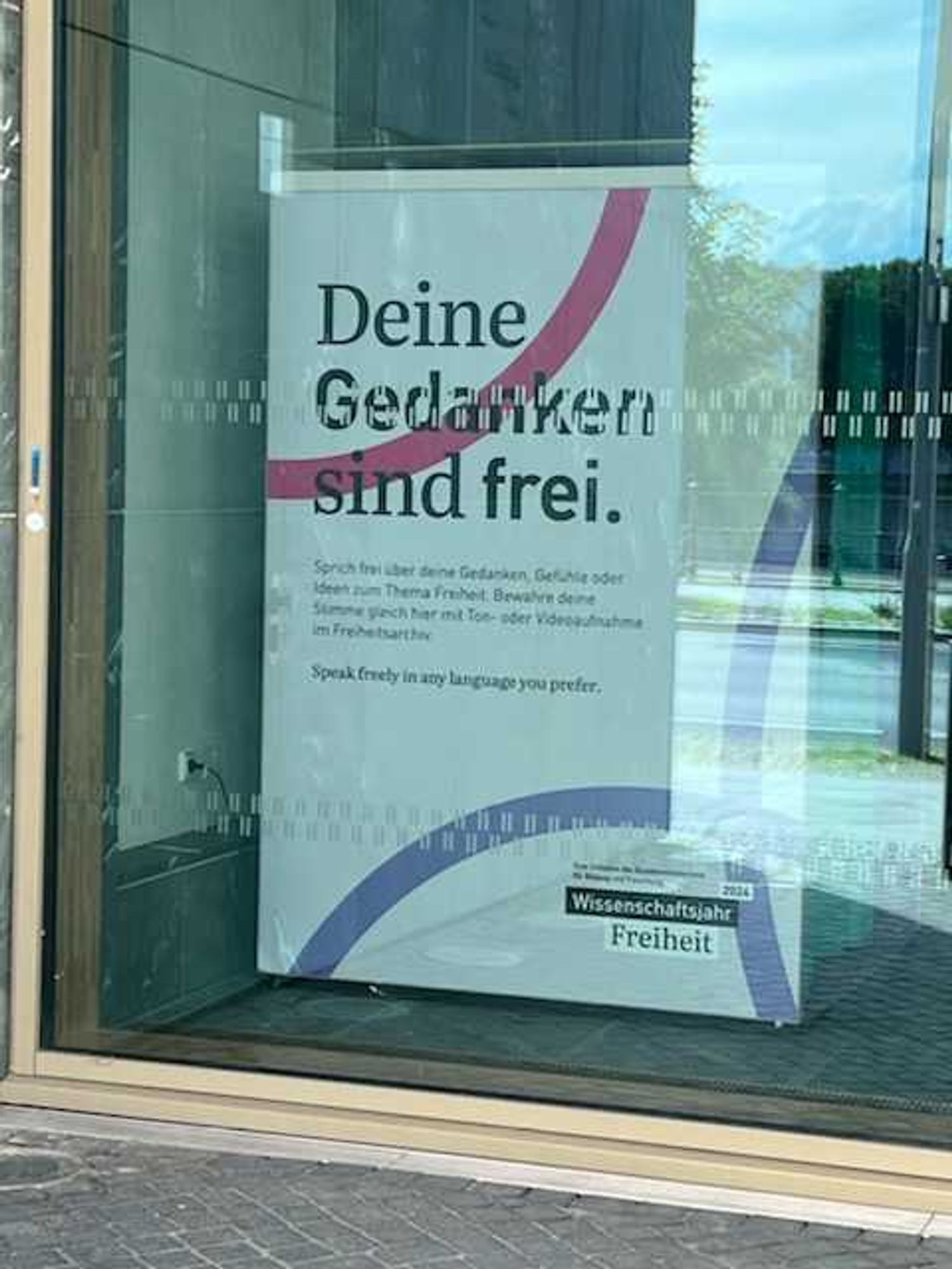 Aufnahme eines großformatigen Aushangs im Foyer des BMBF (Berlin): "Deine Gedanken sind frei. Sprich frei über Deine Gedanken, Gefühle oder Ideen zum Thema Freiheit. Bewahre Deine Stimme gleich hier mit Ton- oder Videoaufnahme im Freiheitsarchiv. Speak freely in any language you prefer. Wissenschaftsjahr Freiheit 2024"